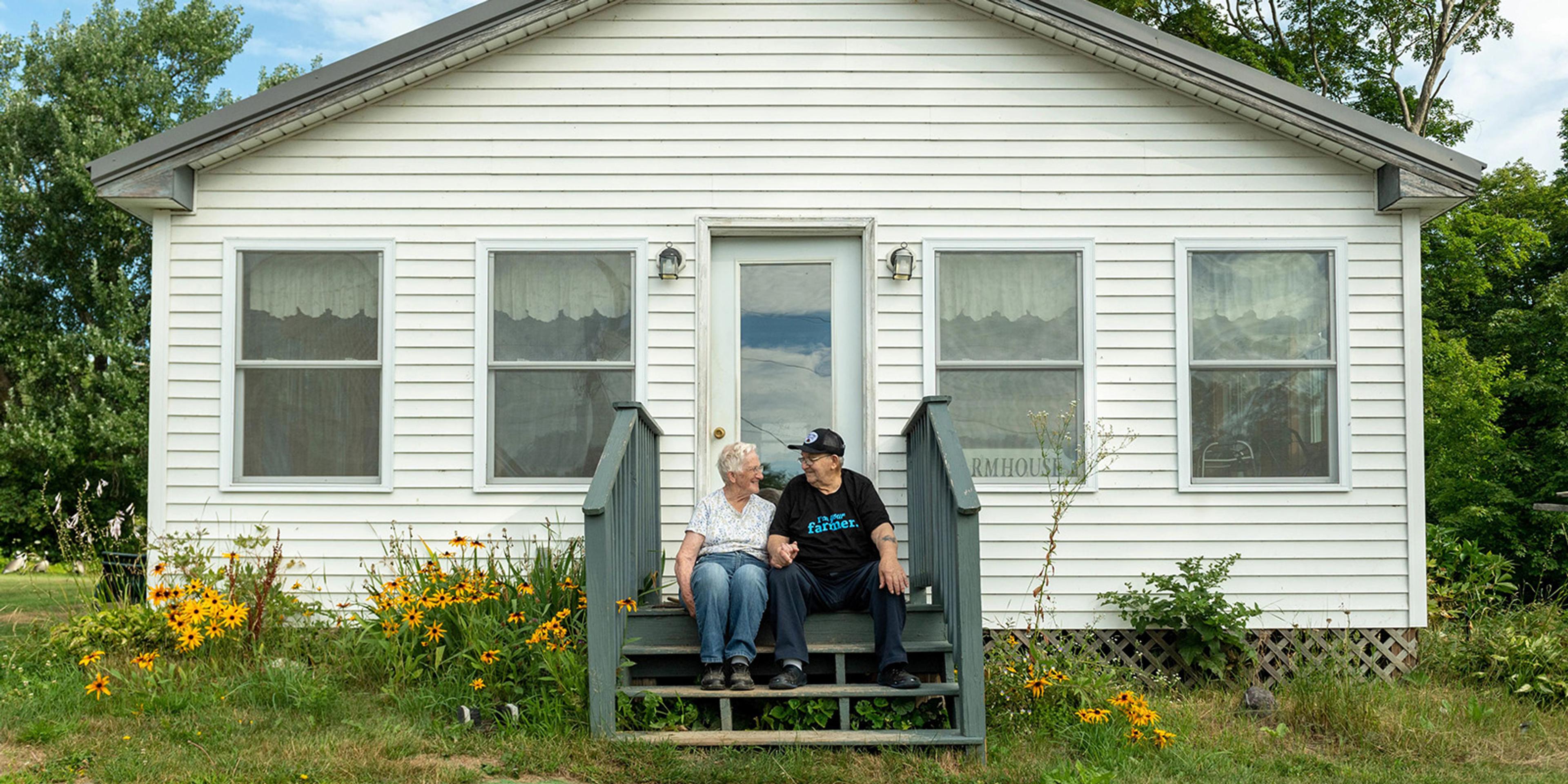 Malcolm and Marilyn Turner sit on their housesteps, which are surrounded by daisies, and smile at their family farm in Maine.