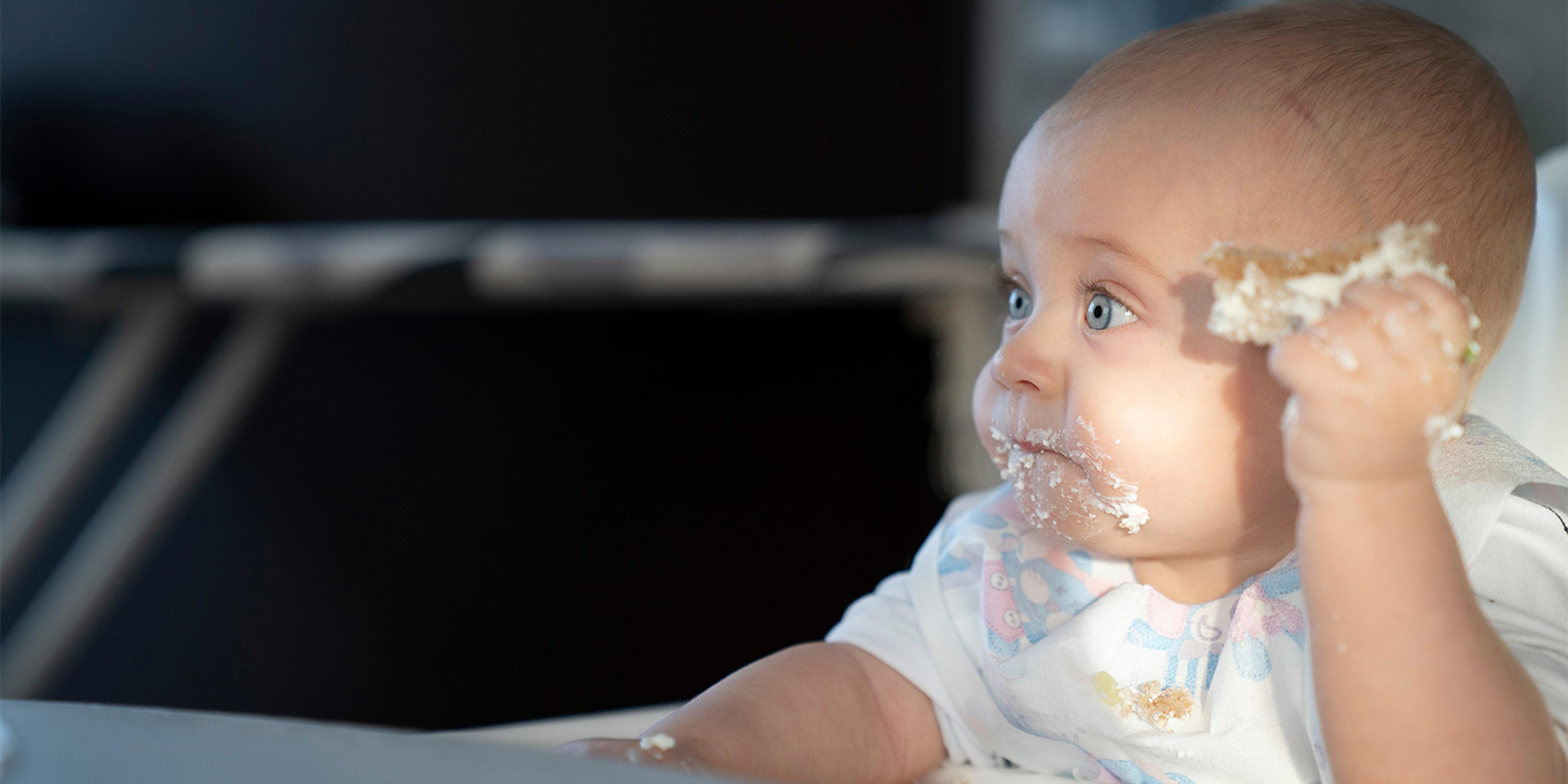 A baby makes a mess eating cottage cheese on toast.