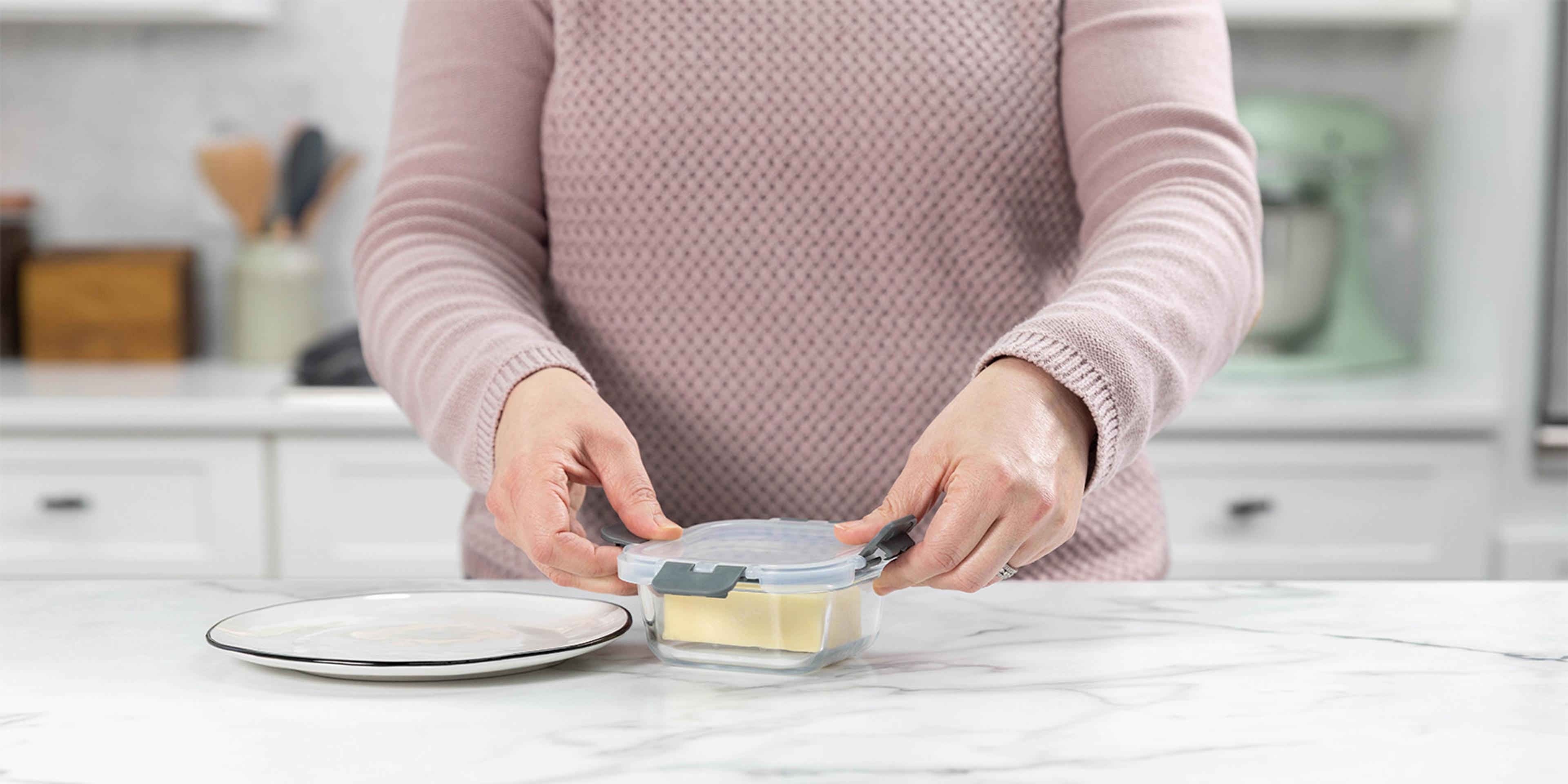 A woman puts cheese in an airtight container.