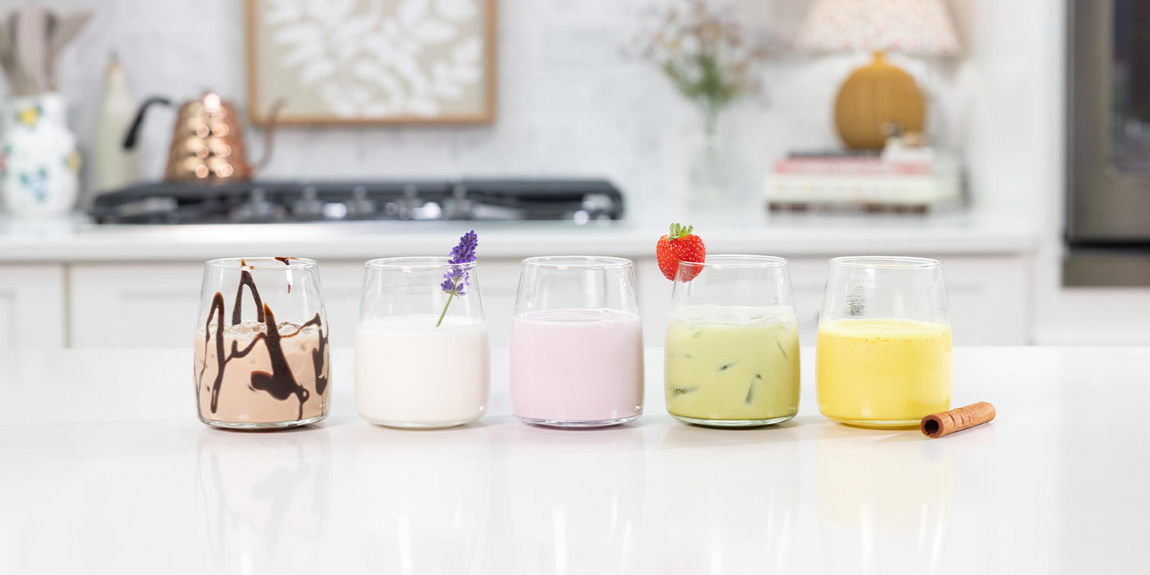 Five glasses of milk using various recipes on a granite kitchen counter.