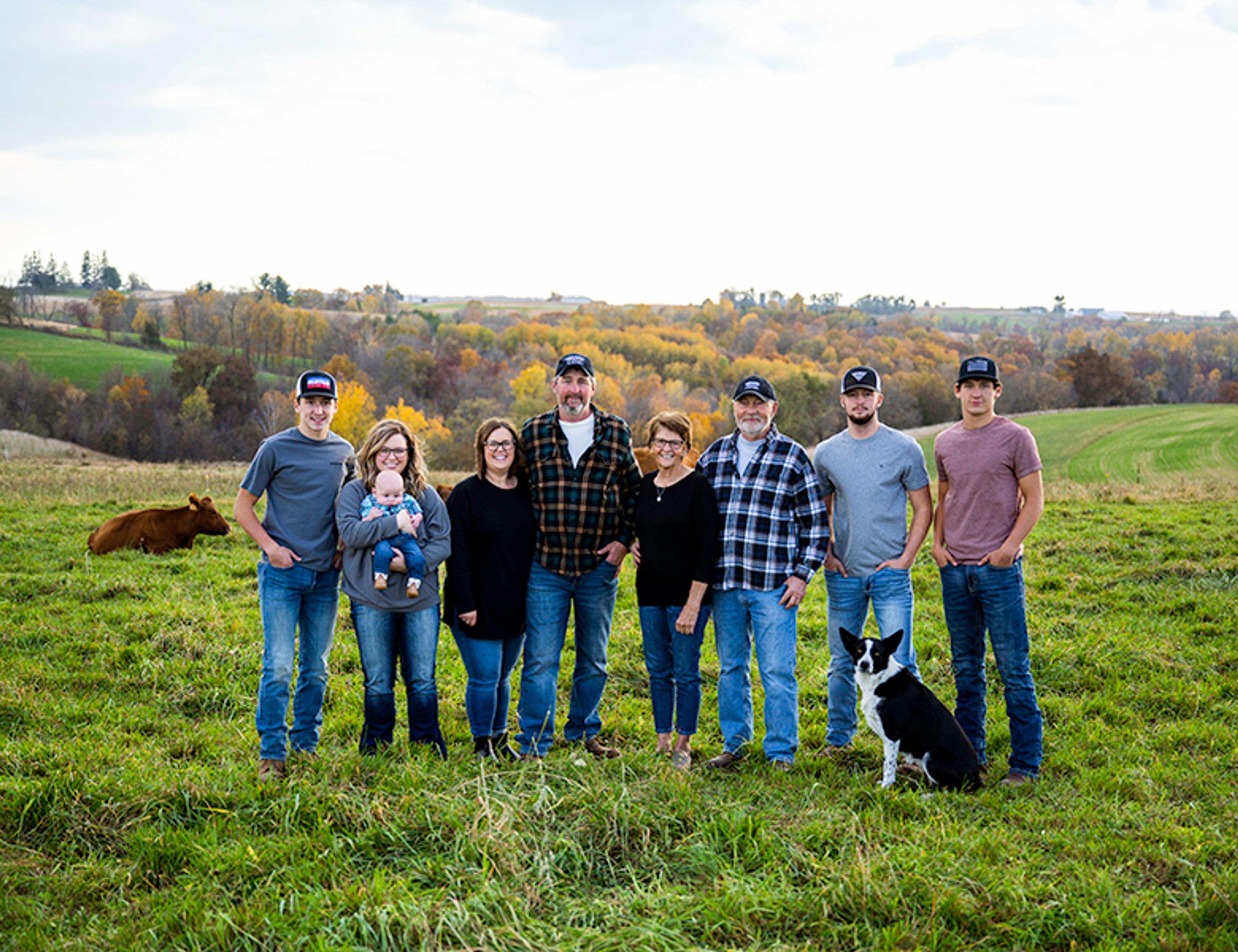 Family Farmers together with farm dog in cow pasture with fall colors on trees.