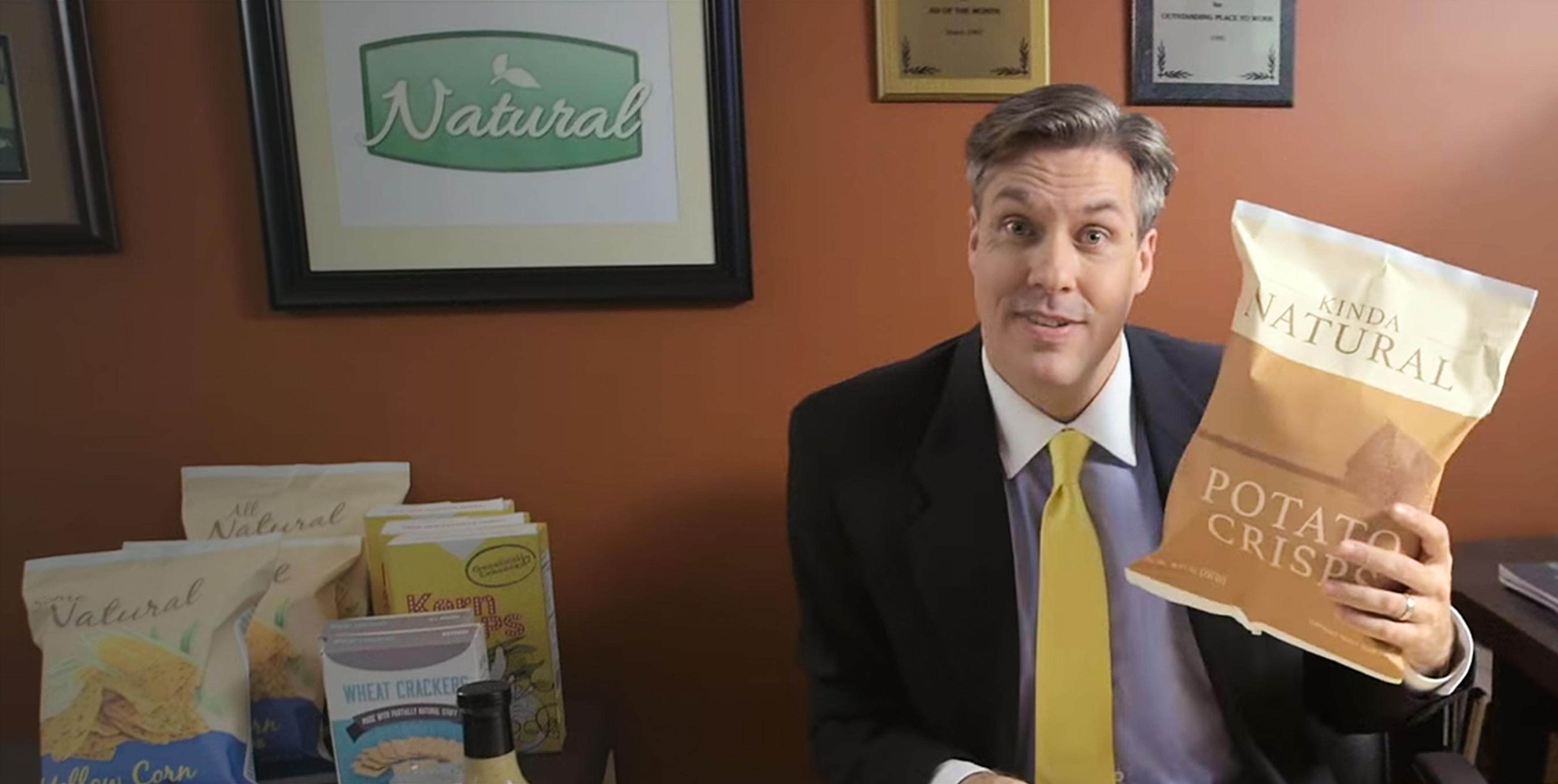 A man in a suit holding a bag of "Kinda Natural Potato Crisps".