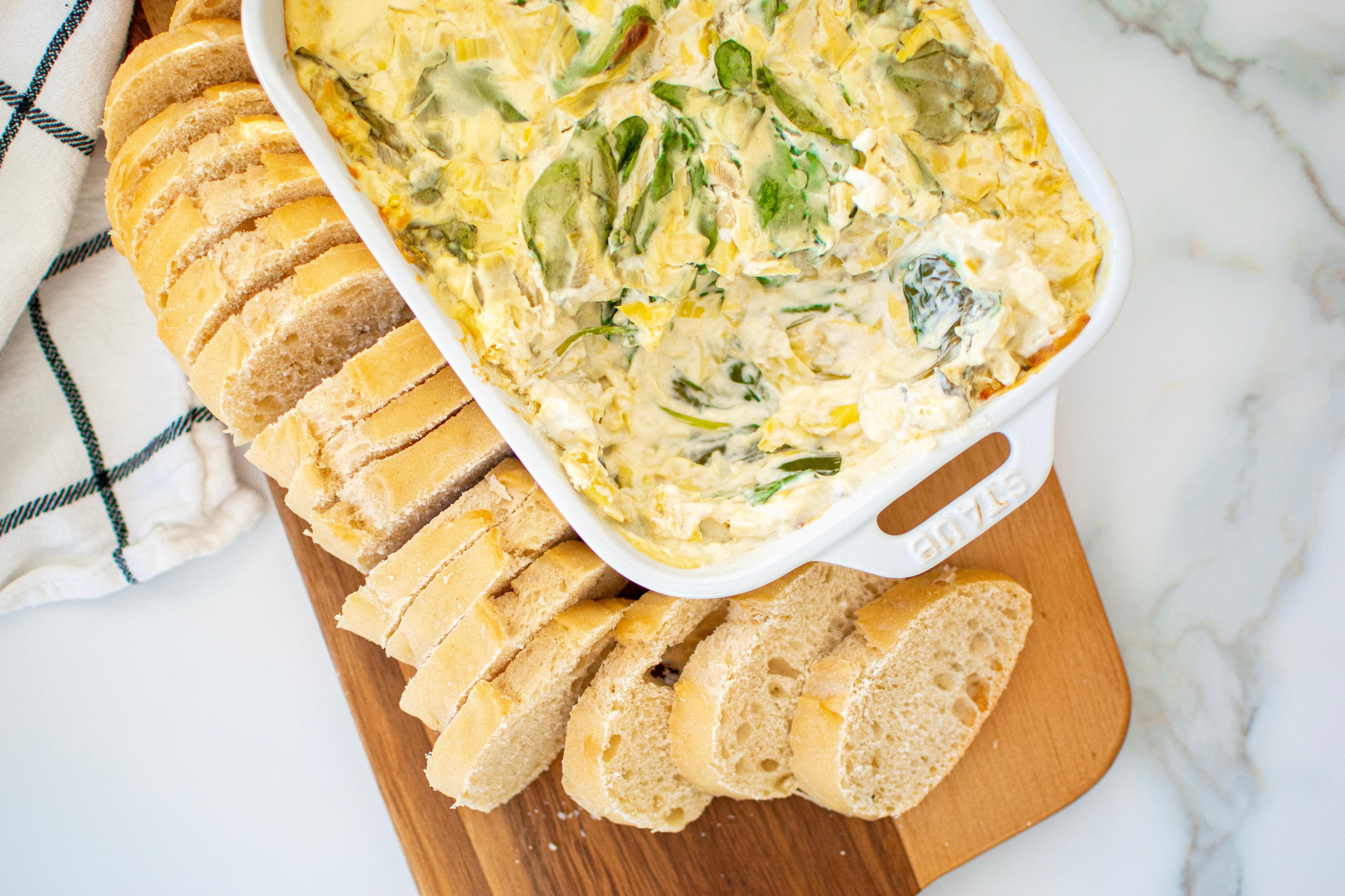 Spinach Artichoke Dip on a cutting board with bread.