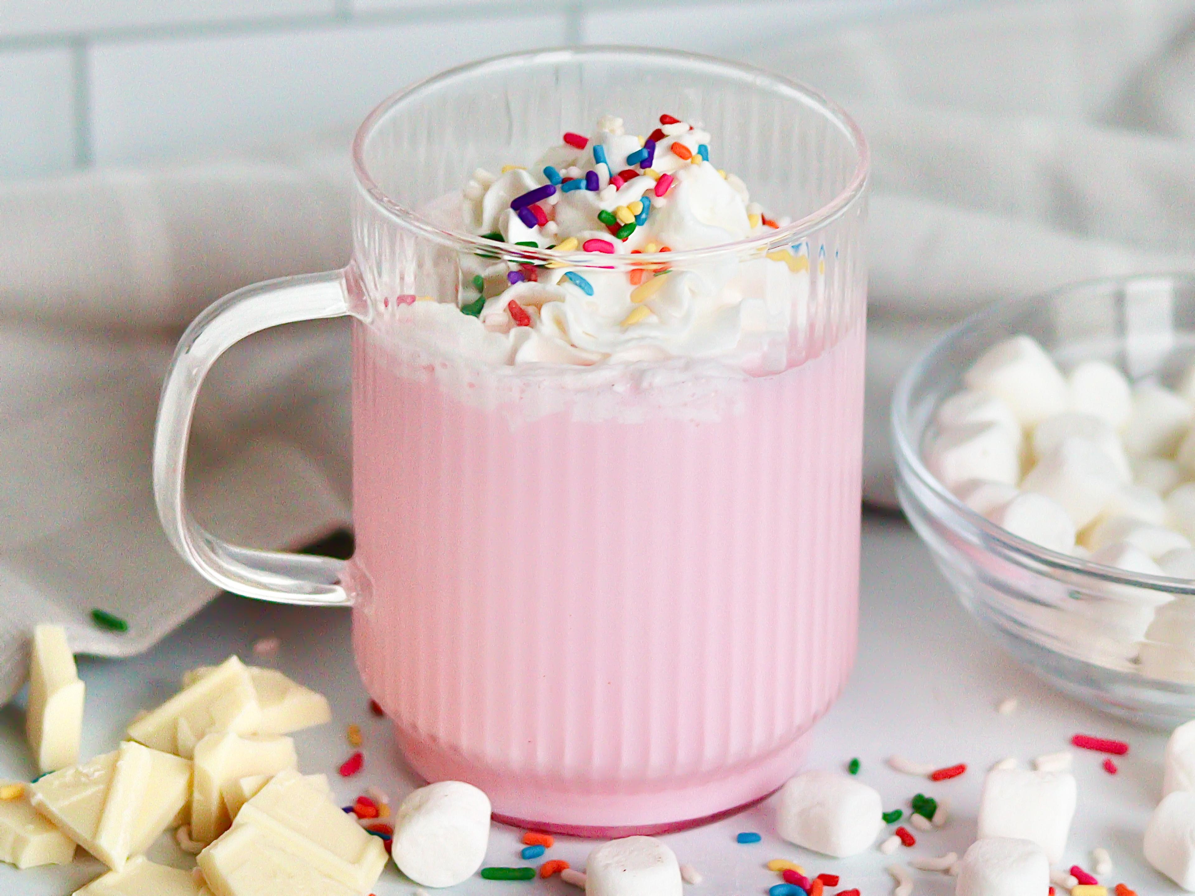 A mug of pink unicorn hot chocolate with marshmallows, sprinkles and whipped cream.