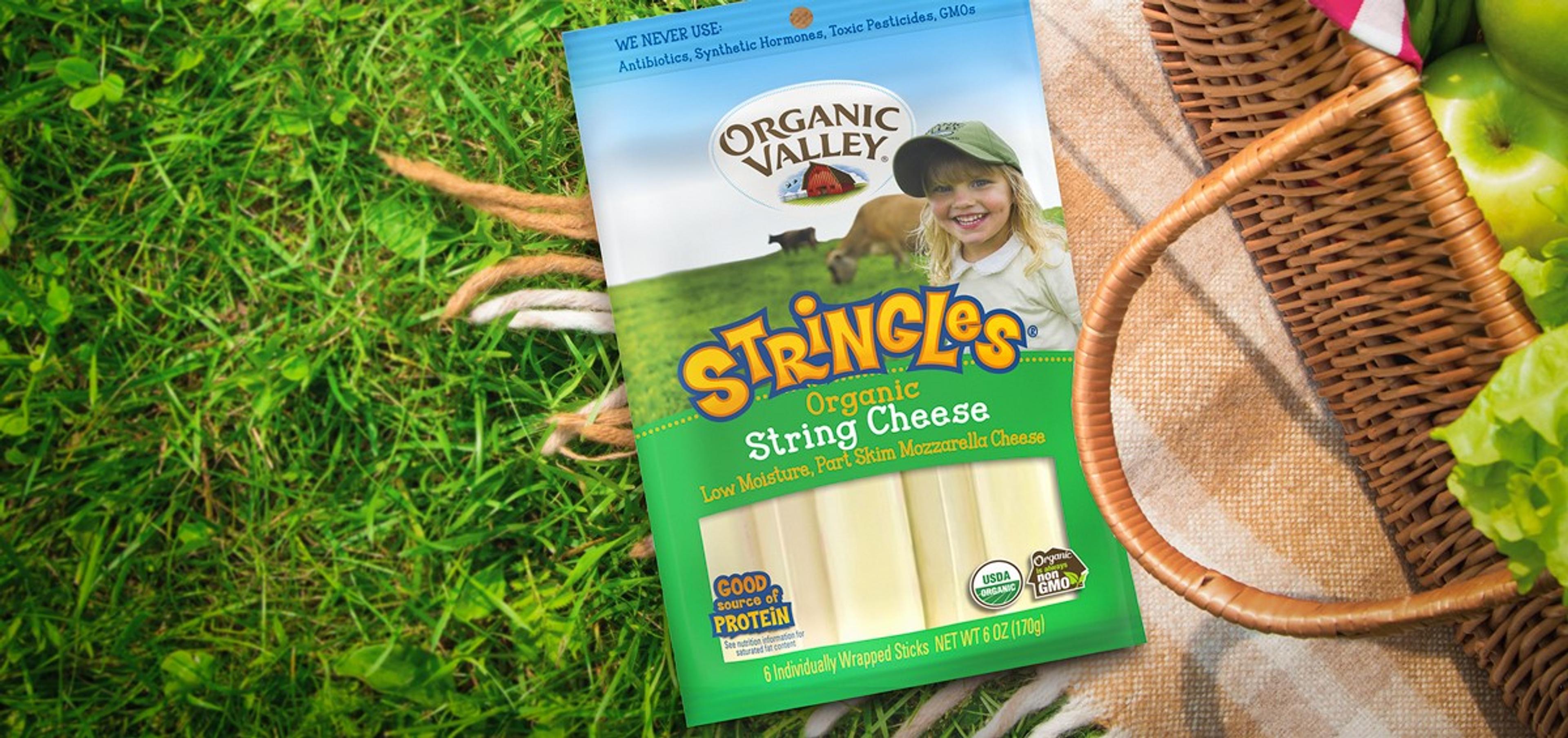 A package of Stringles organic string cheese on a blanket next to a picnic basket.