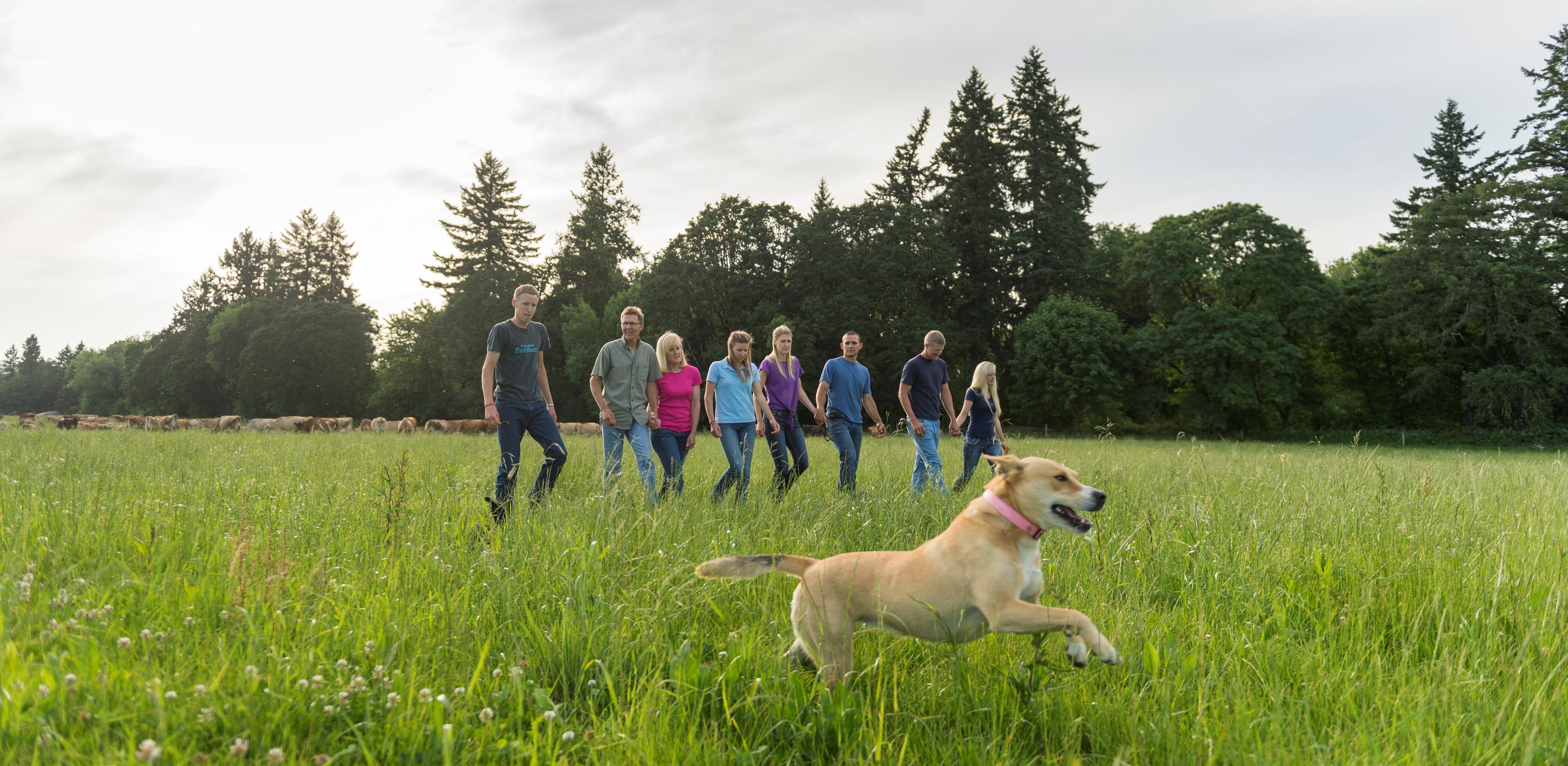 A dog leads the way as the Bansen family walks in the pasture.
