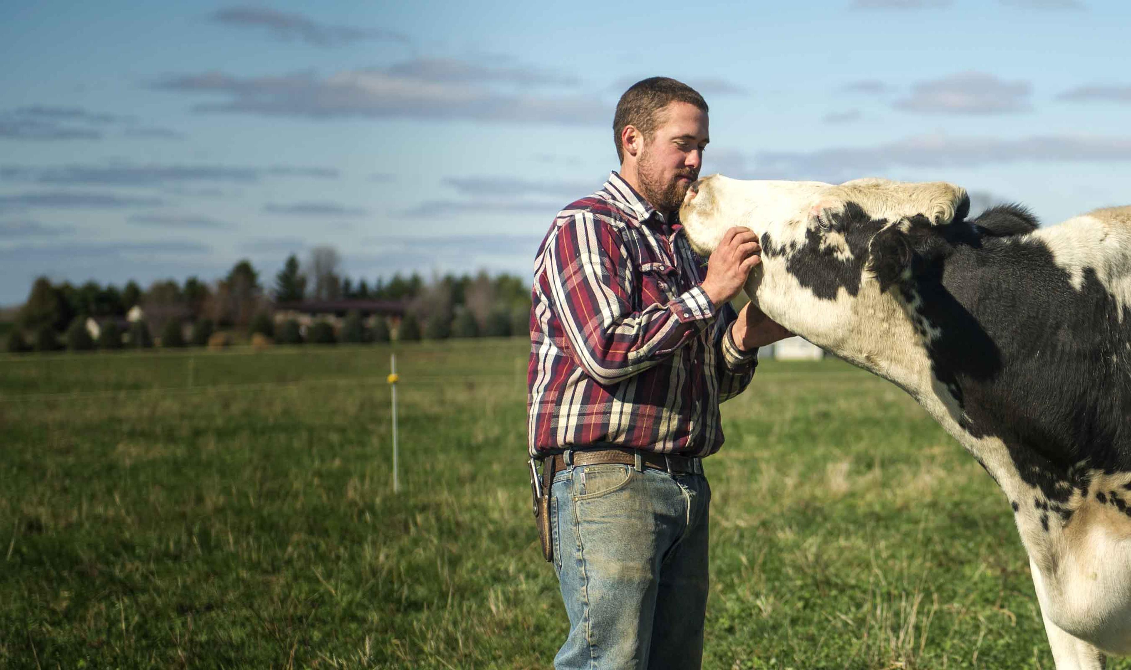 A farmer standing with his cow in the field.