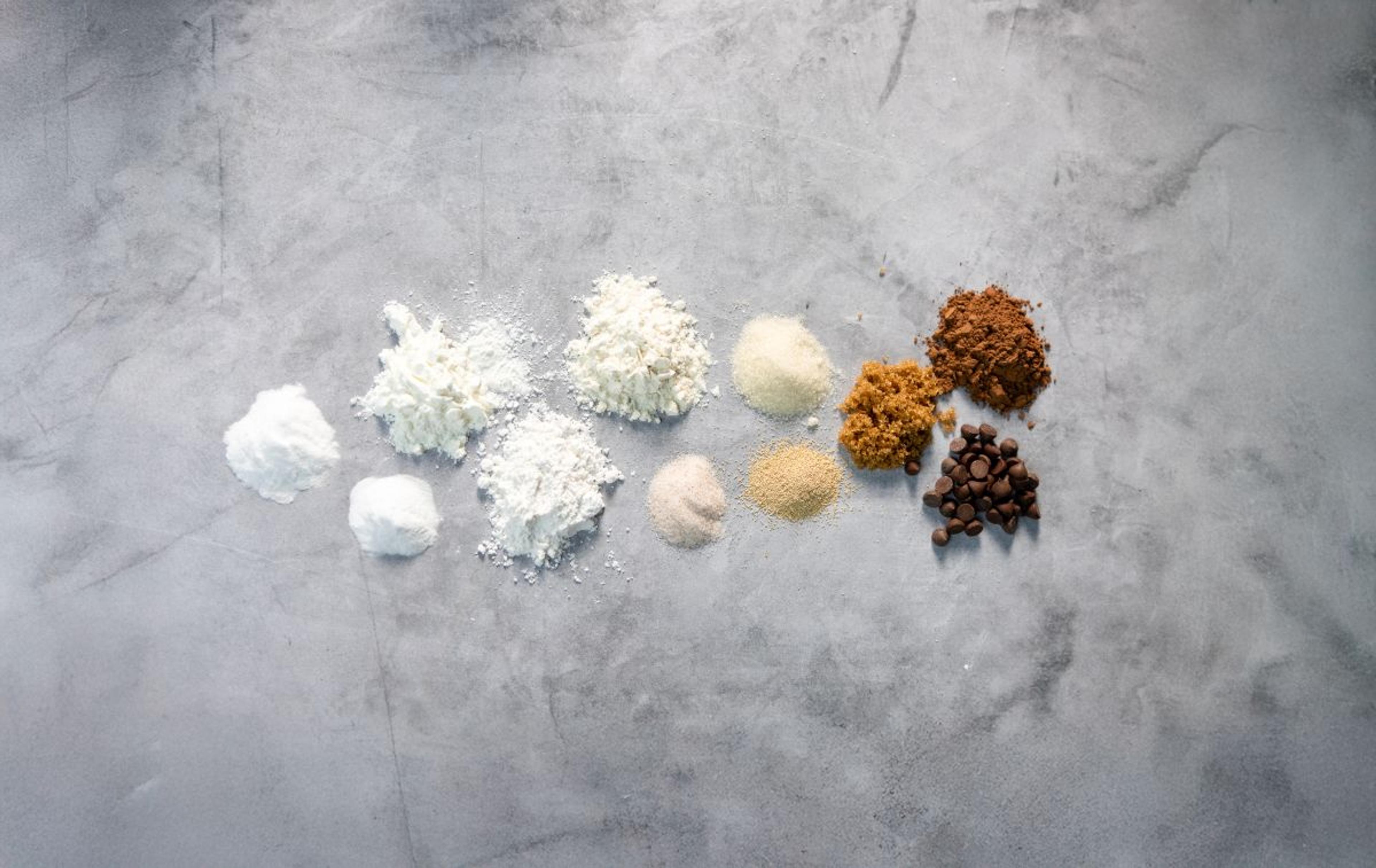 Chocolate chips, brown sugar, yeast and other ingredients out of their packages on a white background.