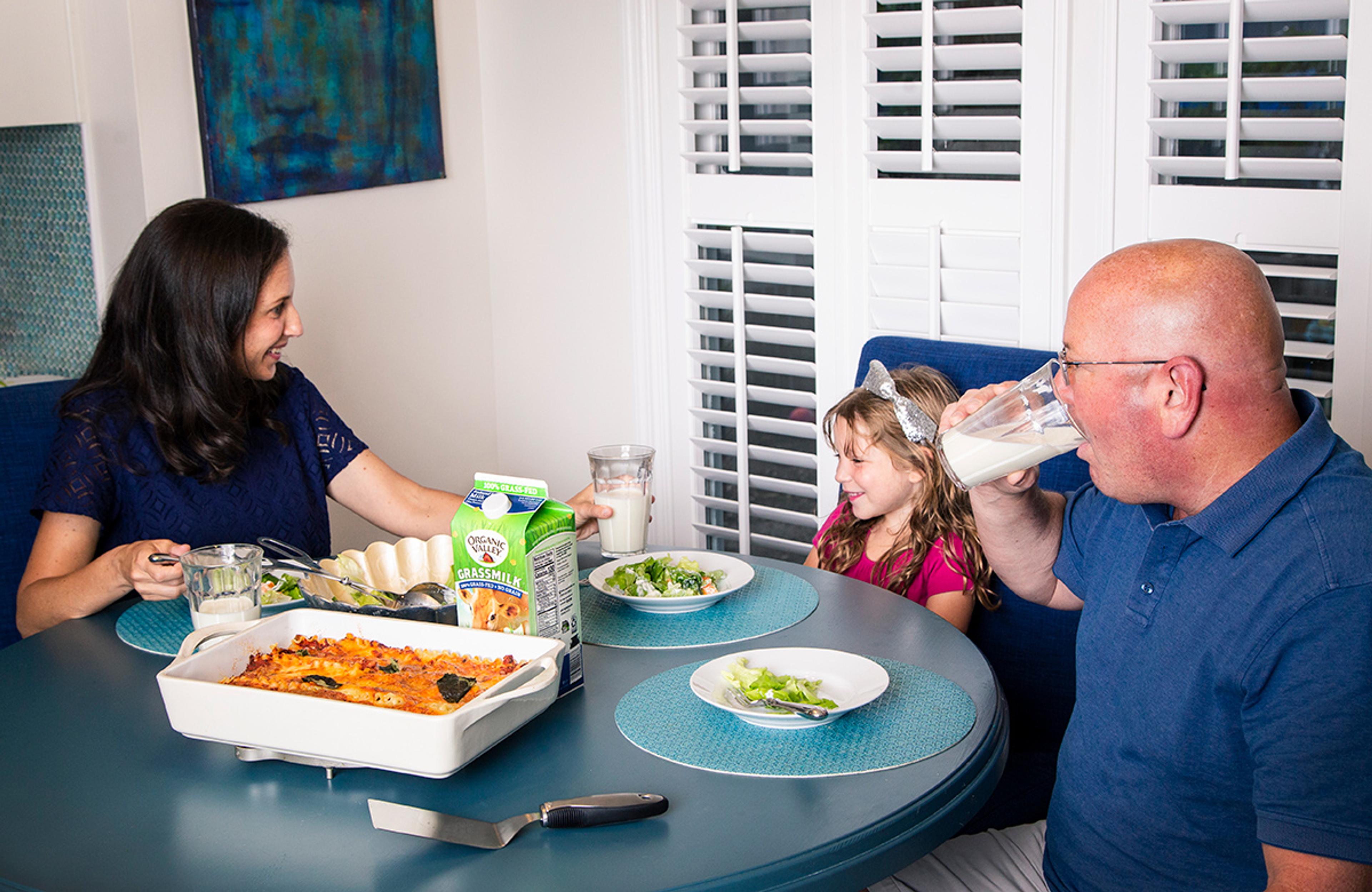 A mom, dad, and daughter enjoy a meal of lasagna, salad, and Organic Valley Grassmilk.