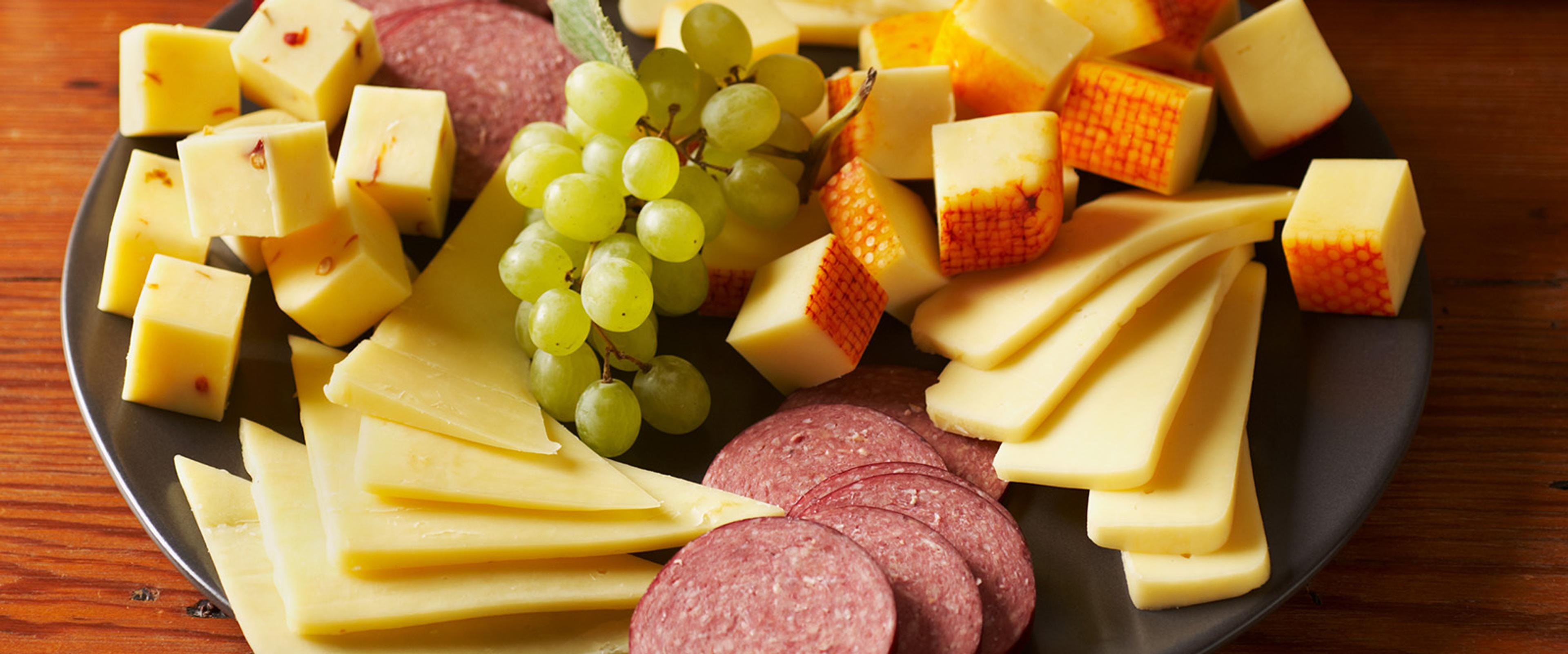 A tray of cheese, sausage, and grapes
