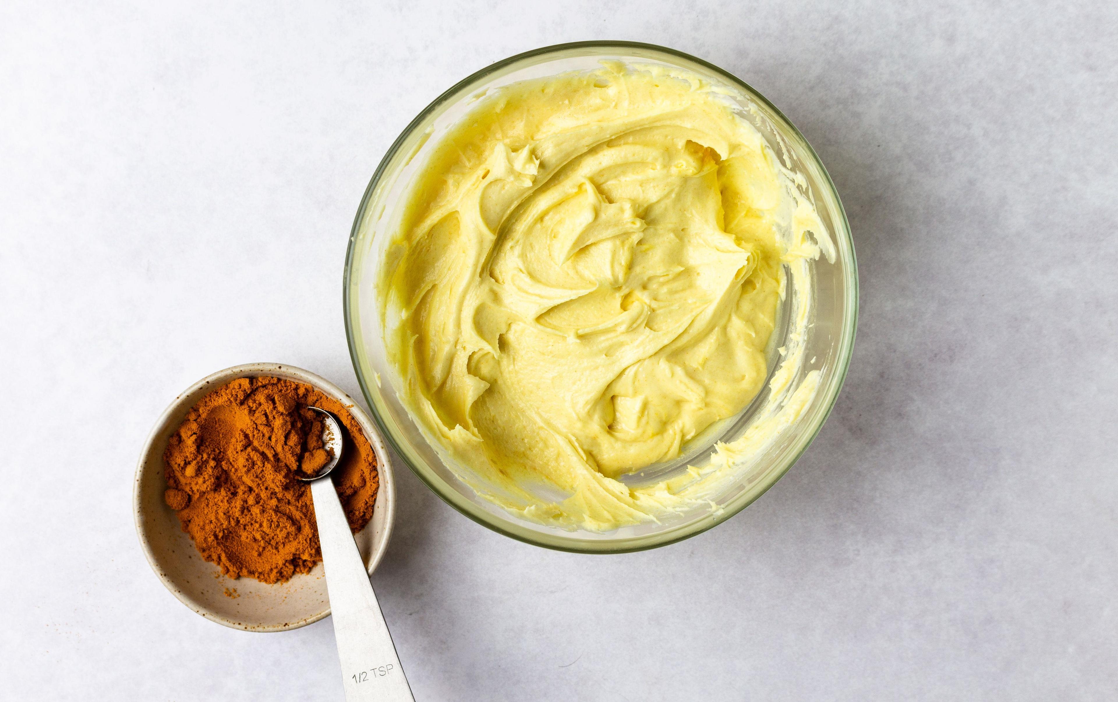 Turmeric next to a bowl of frosting with turmeric mixed in to create yellow frosting..