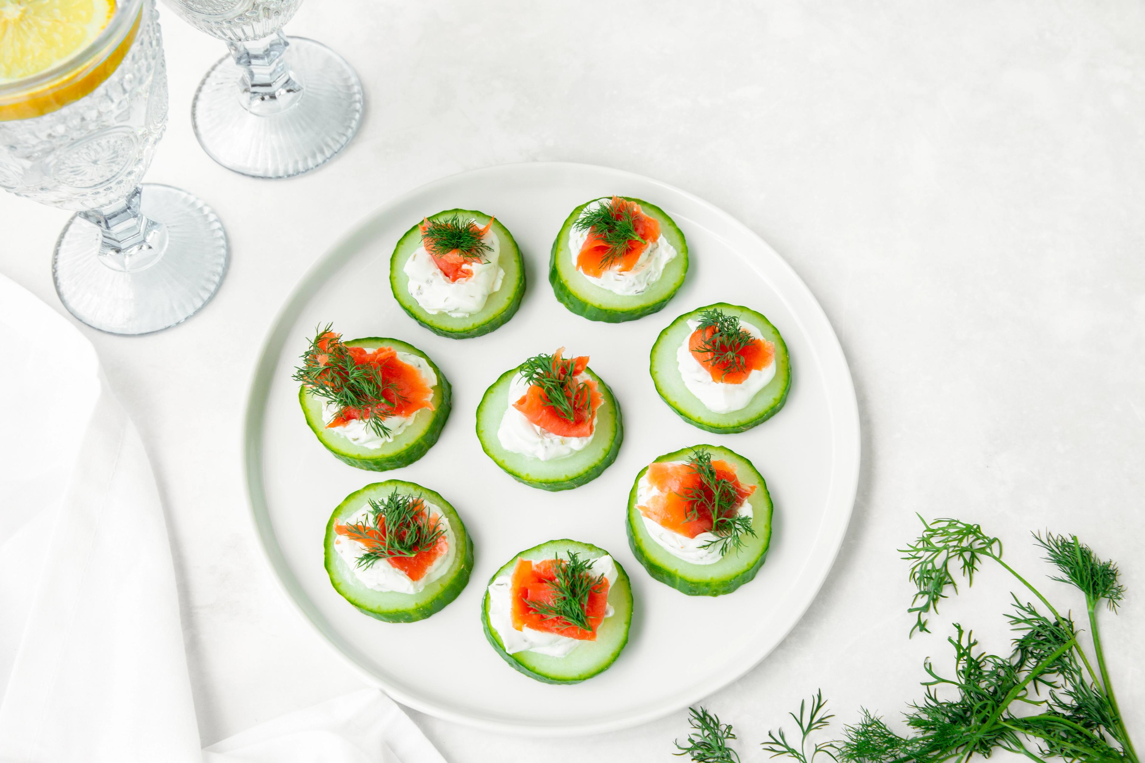 A smoked salmon cucumber appetizer next to dill and glasses of water with lemon slice. 