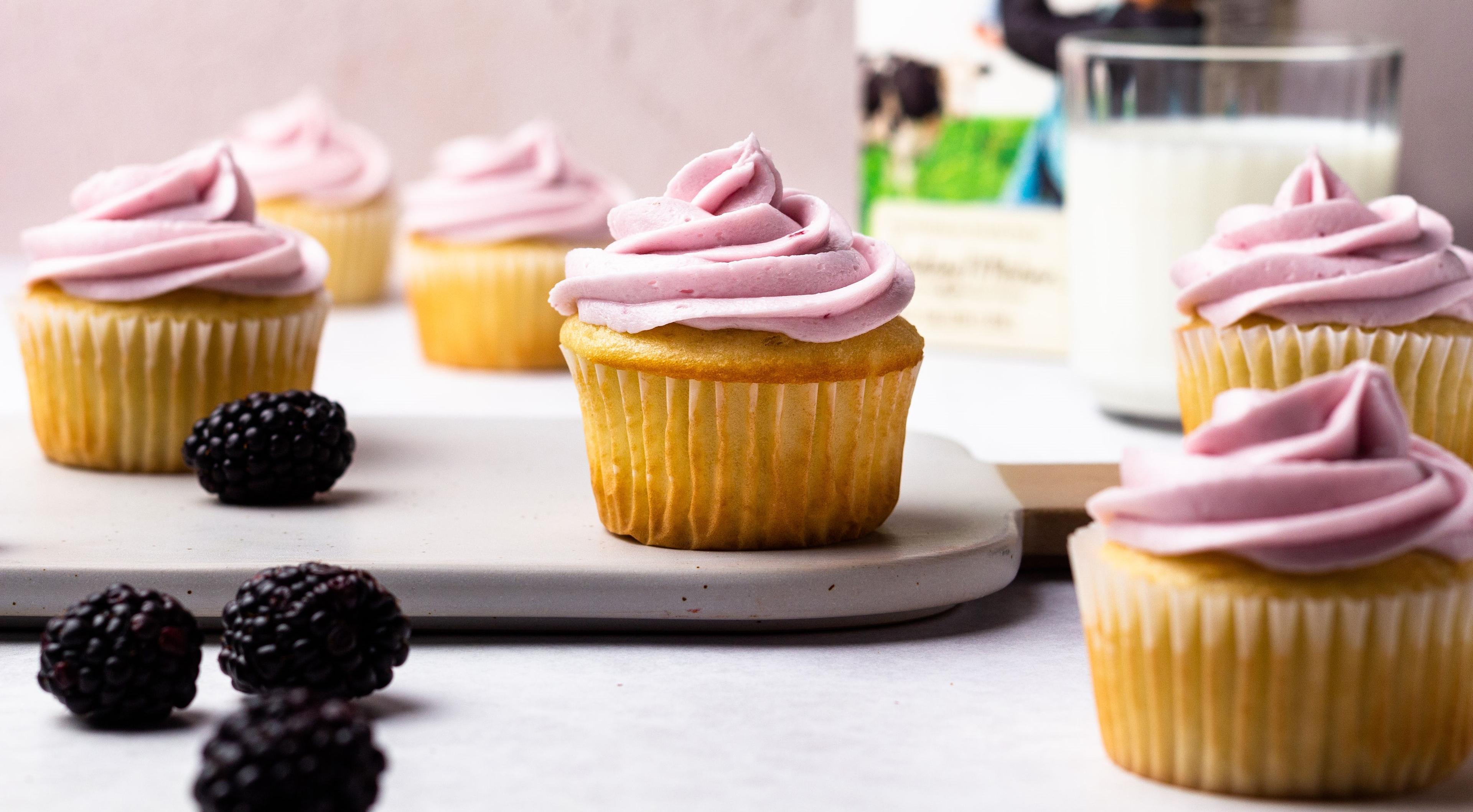 Fresh blackberries next to cupcakes with purple frosting.