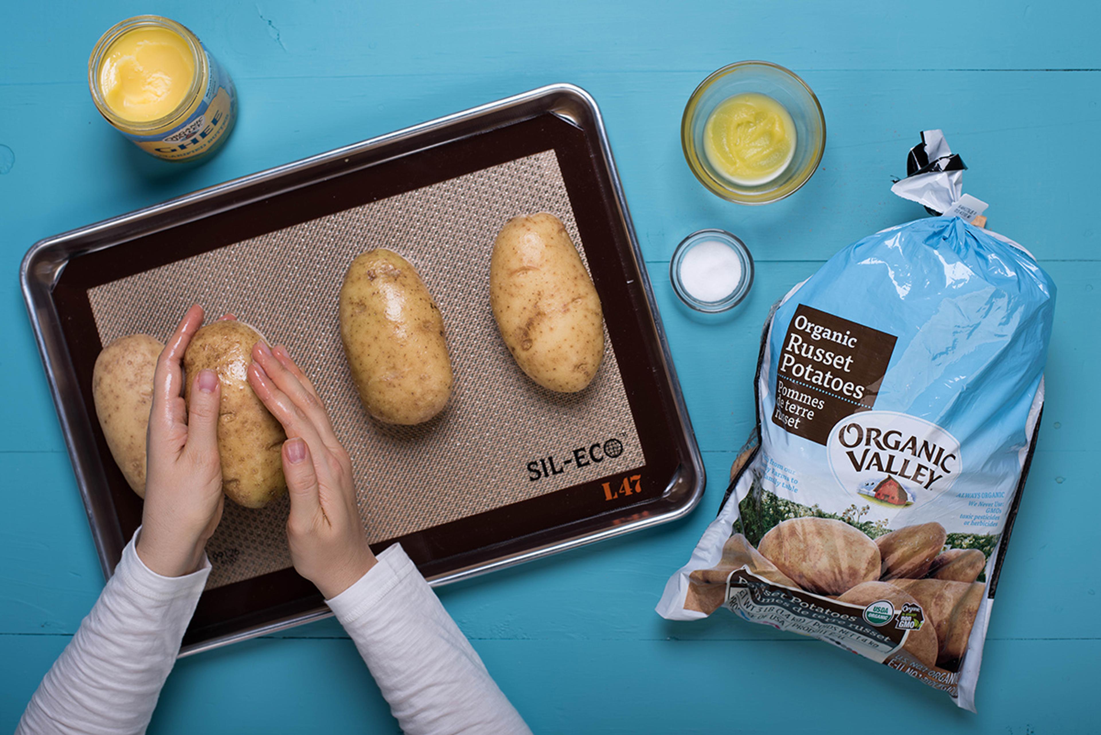 Organic potatoes are spread with Organic Valley Ghee on a baking sheet.
