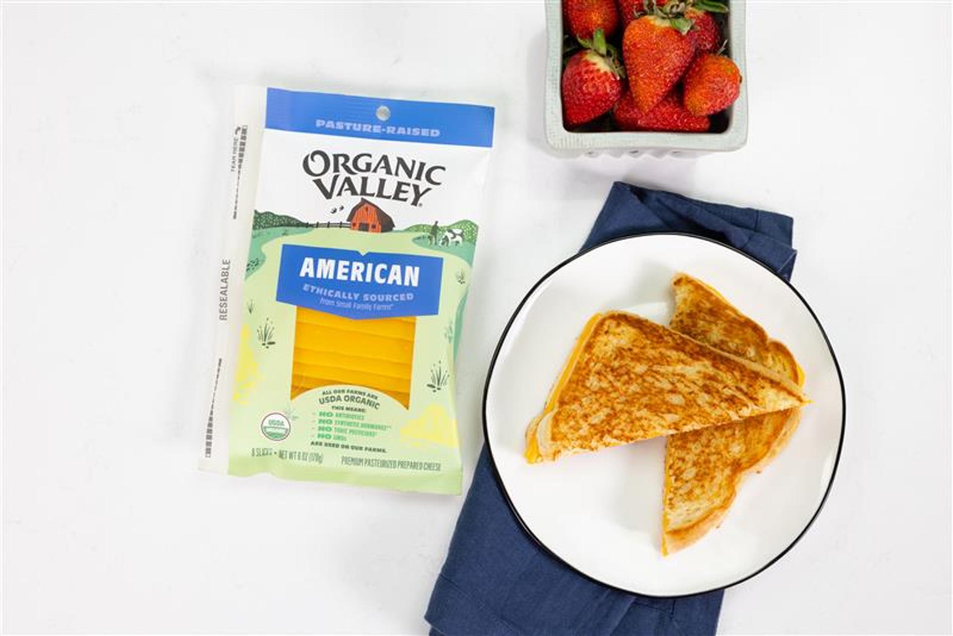 A package of Organic Valley American Cheese slices next to a grilled cheese sandwich and strawberries.