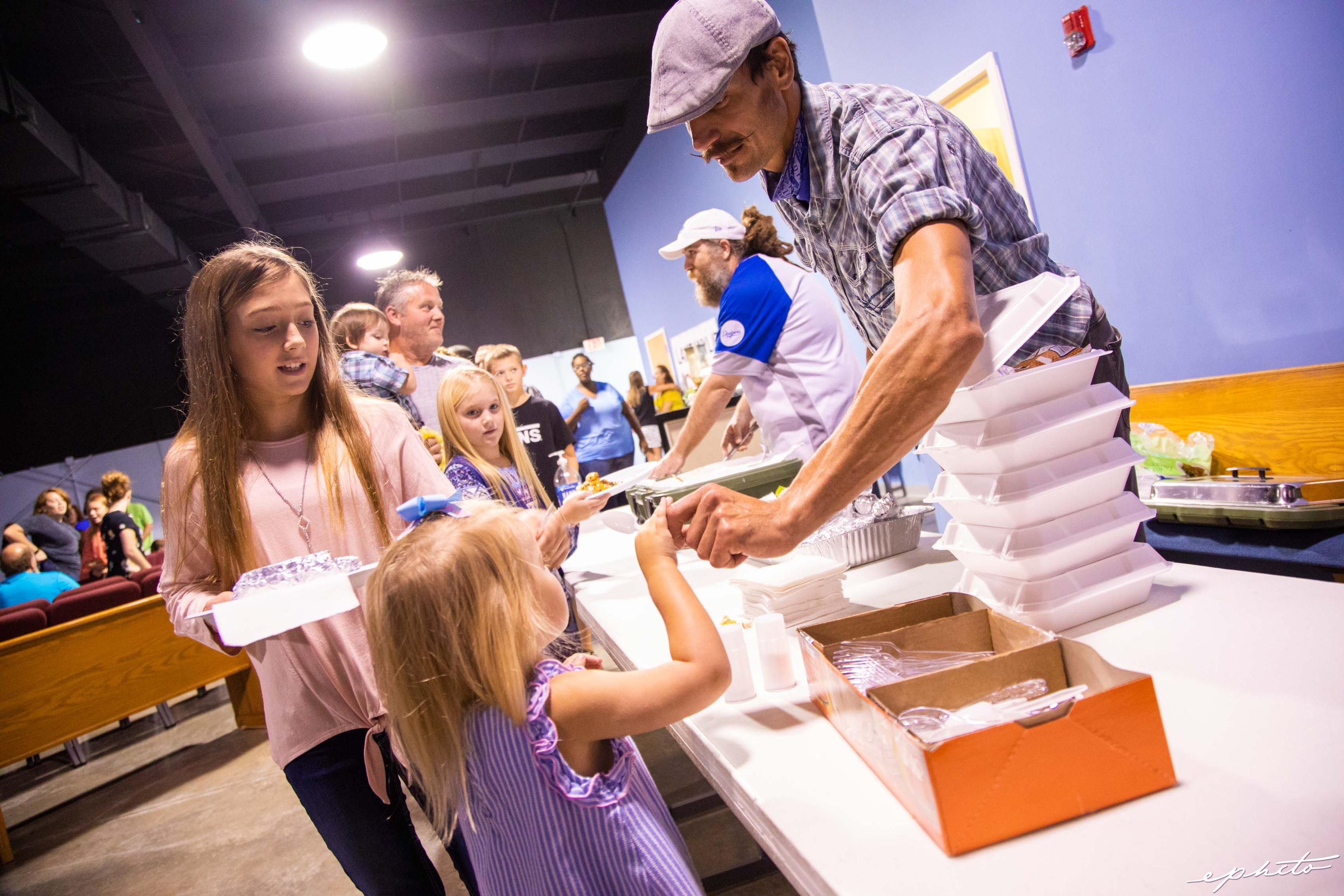 A little girl takes a utensil from a male volunteer in a disaster relief foodservice line.
