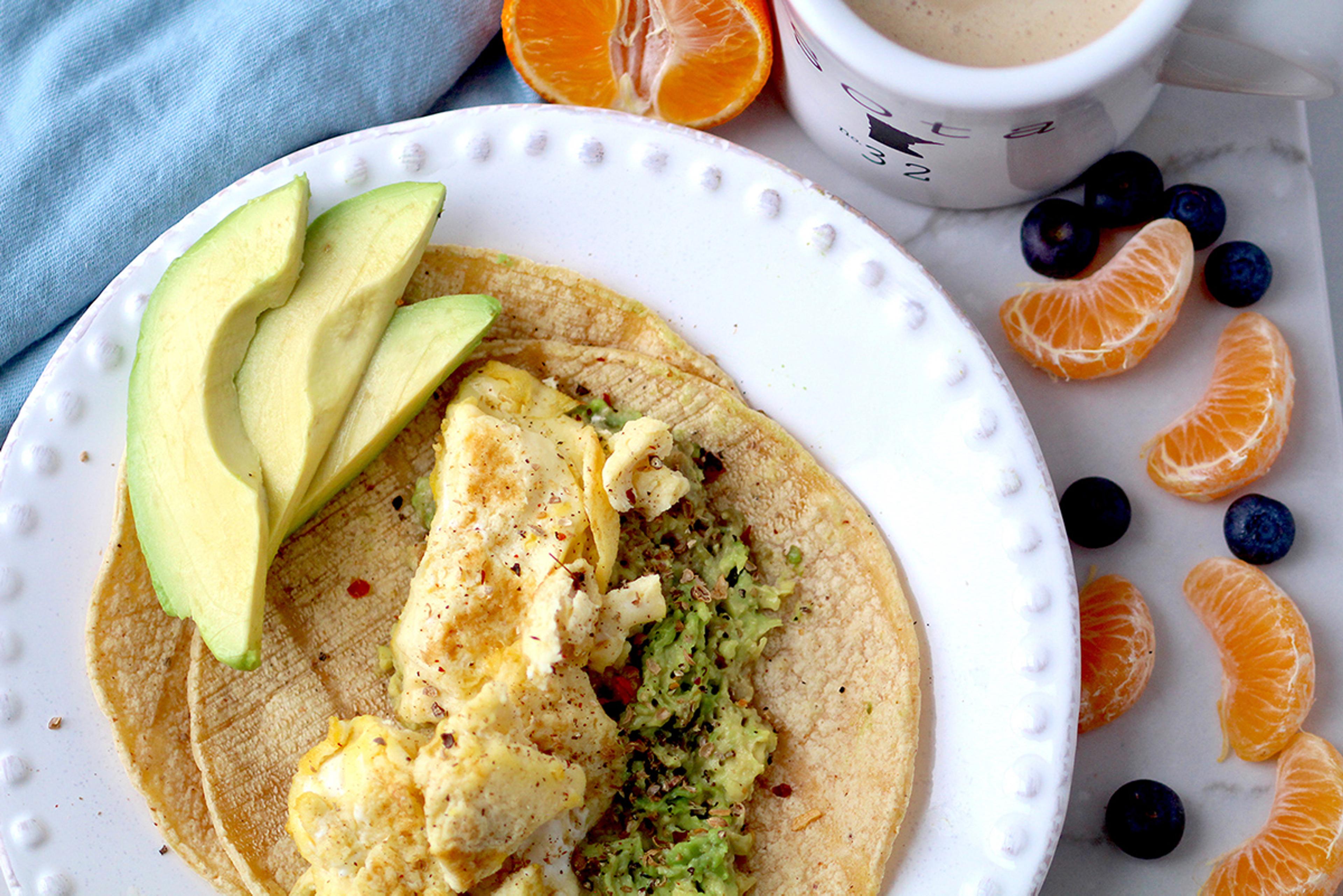 Avocado tortilla egg scramble served with fresh fruit and coffee.