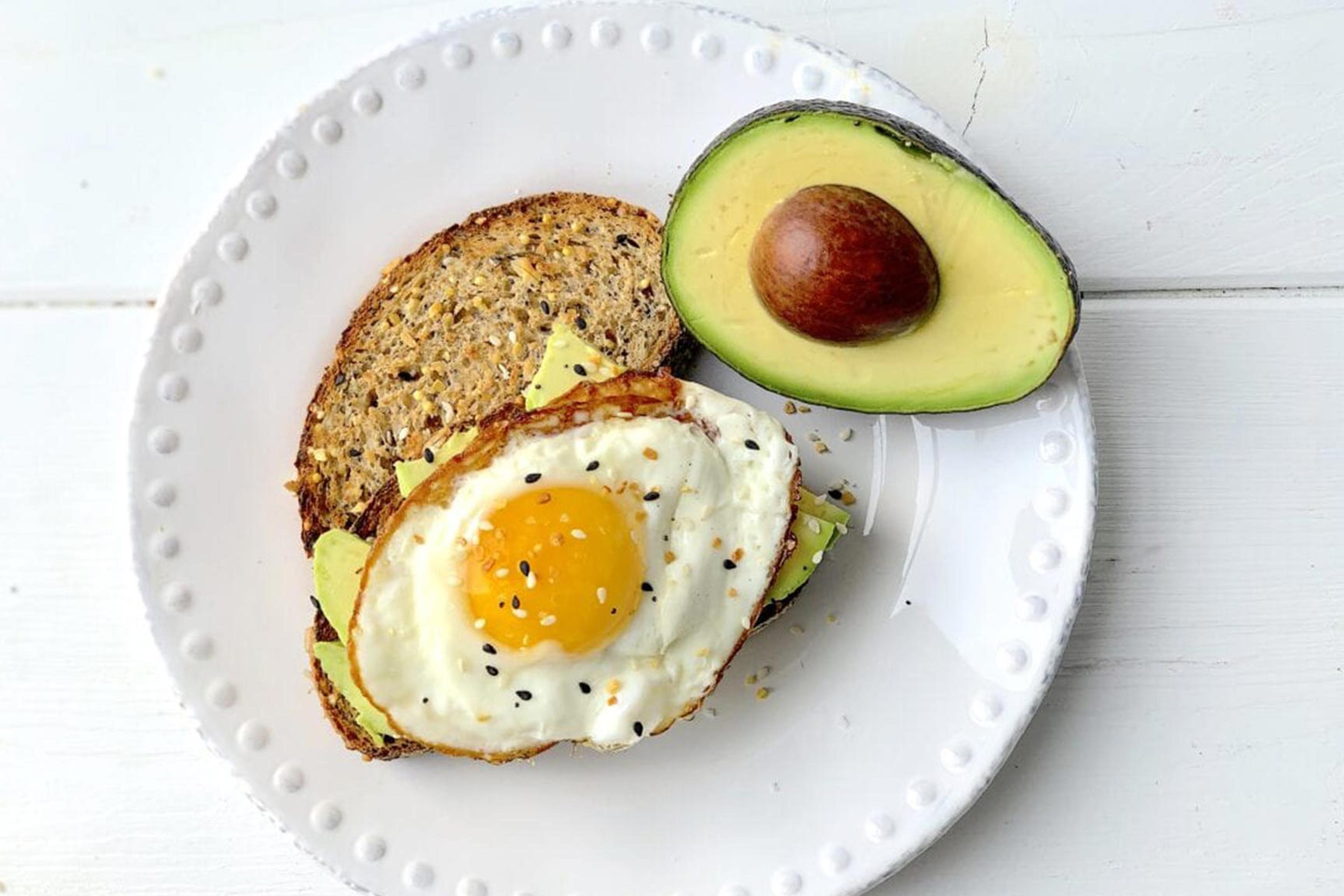An egg dripping golden yolk over avocado toast with alfalfa sprouts.