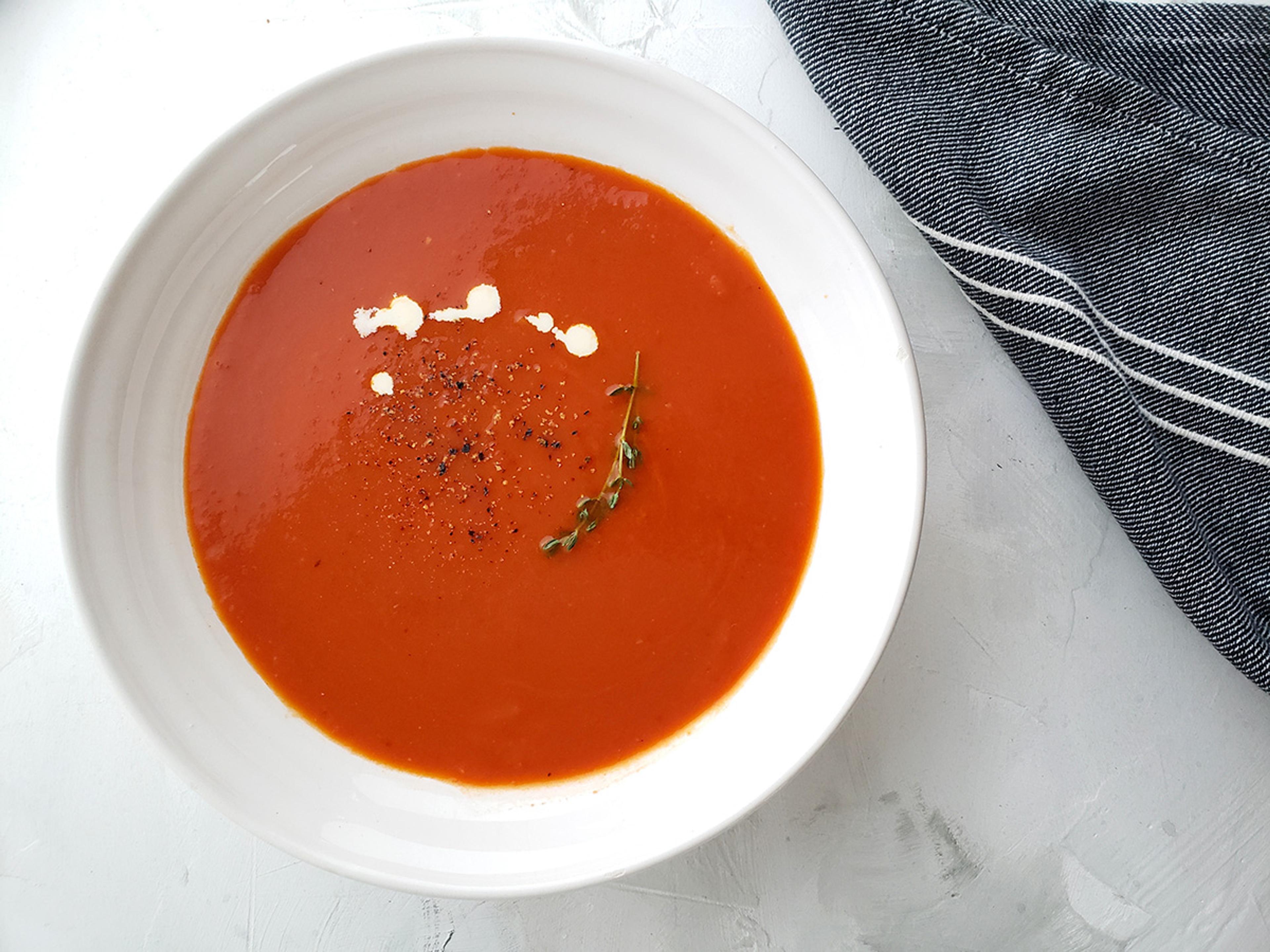 Lovely red tomato soup sprinkled with pepper, a few drops of white cream, and a thyme sprig.