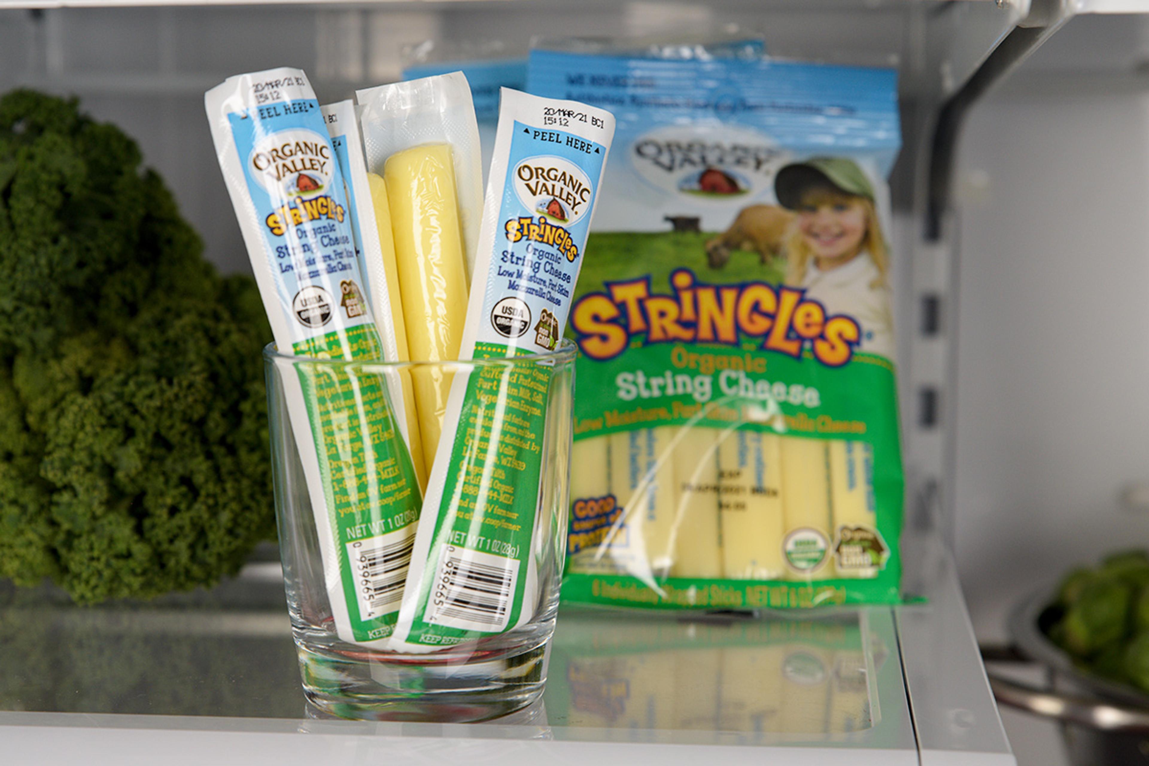 Organic Valley Stringles being held in front of a stocked fridge.