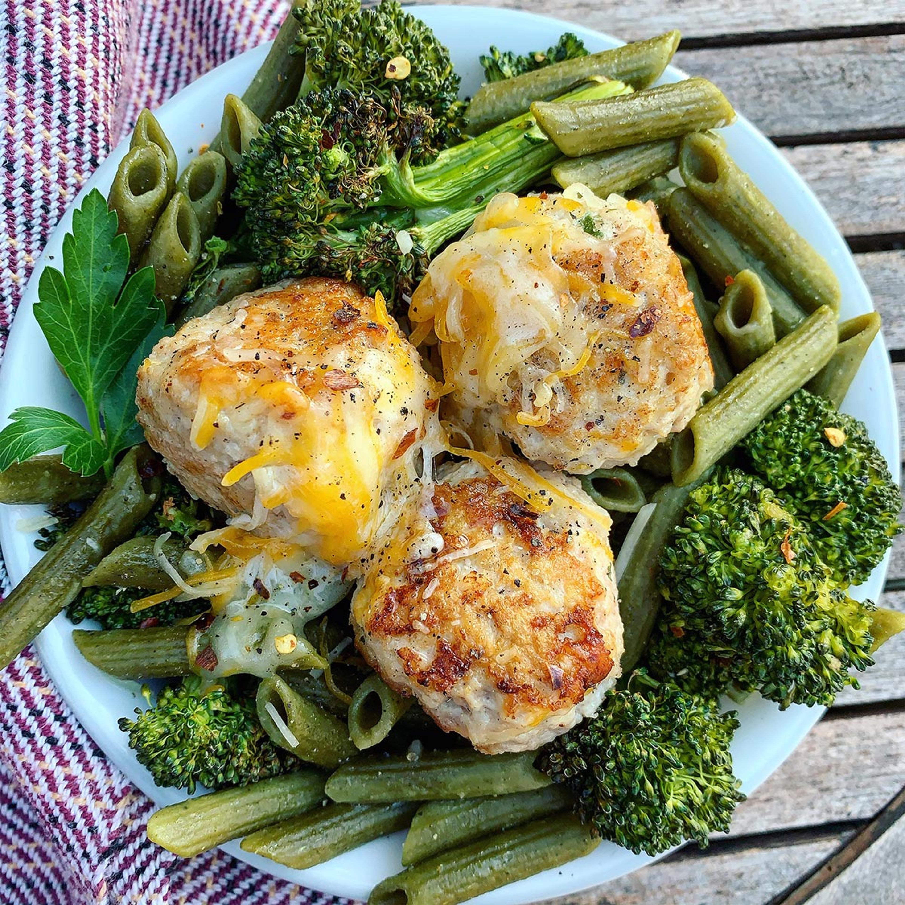 Three chicken meatballs topped with cheese sit atop a bed of green pasta and broccoli.