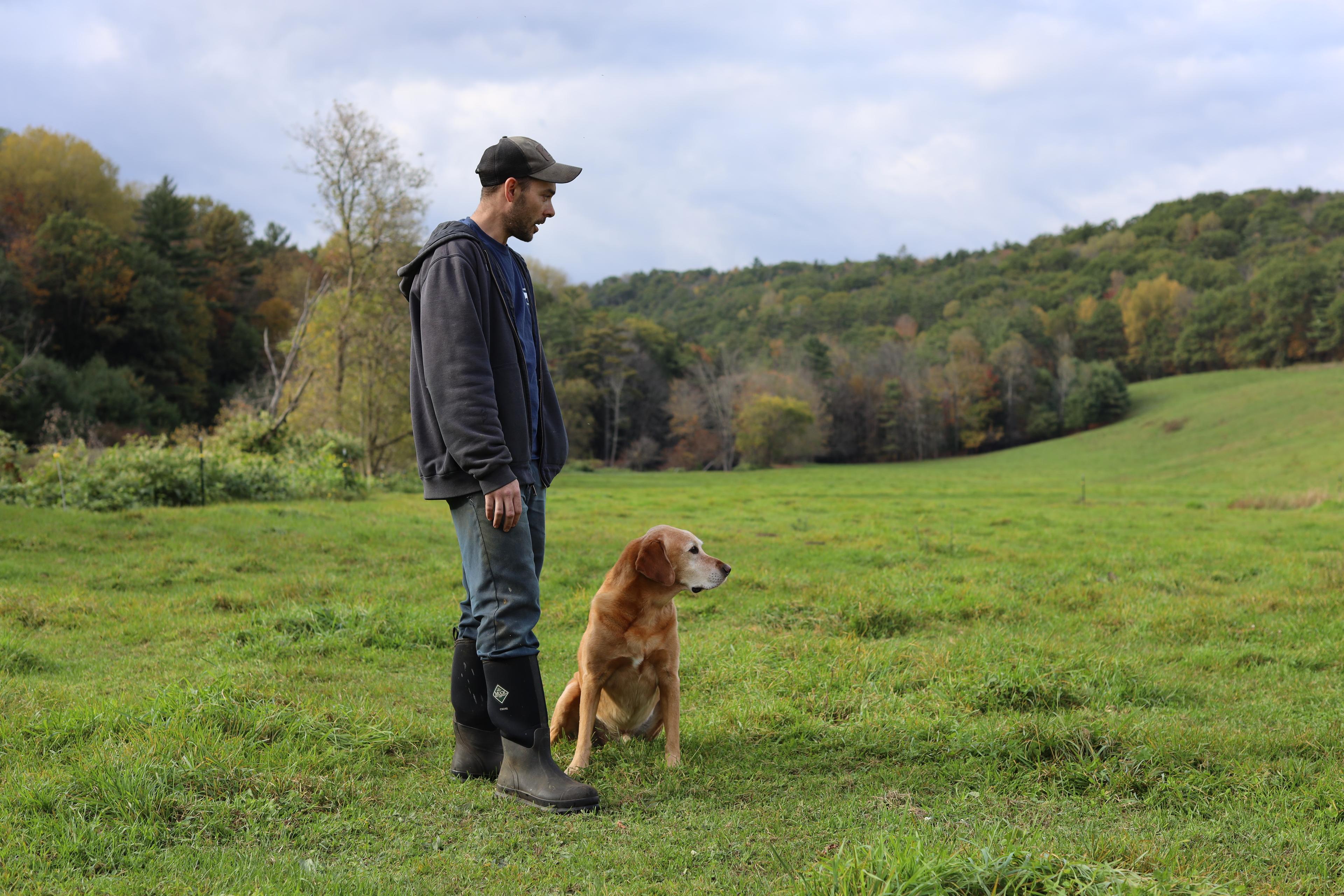 Kyle Leibold and his dog stand in a pasture on their organic farm.