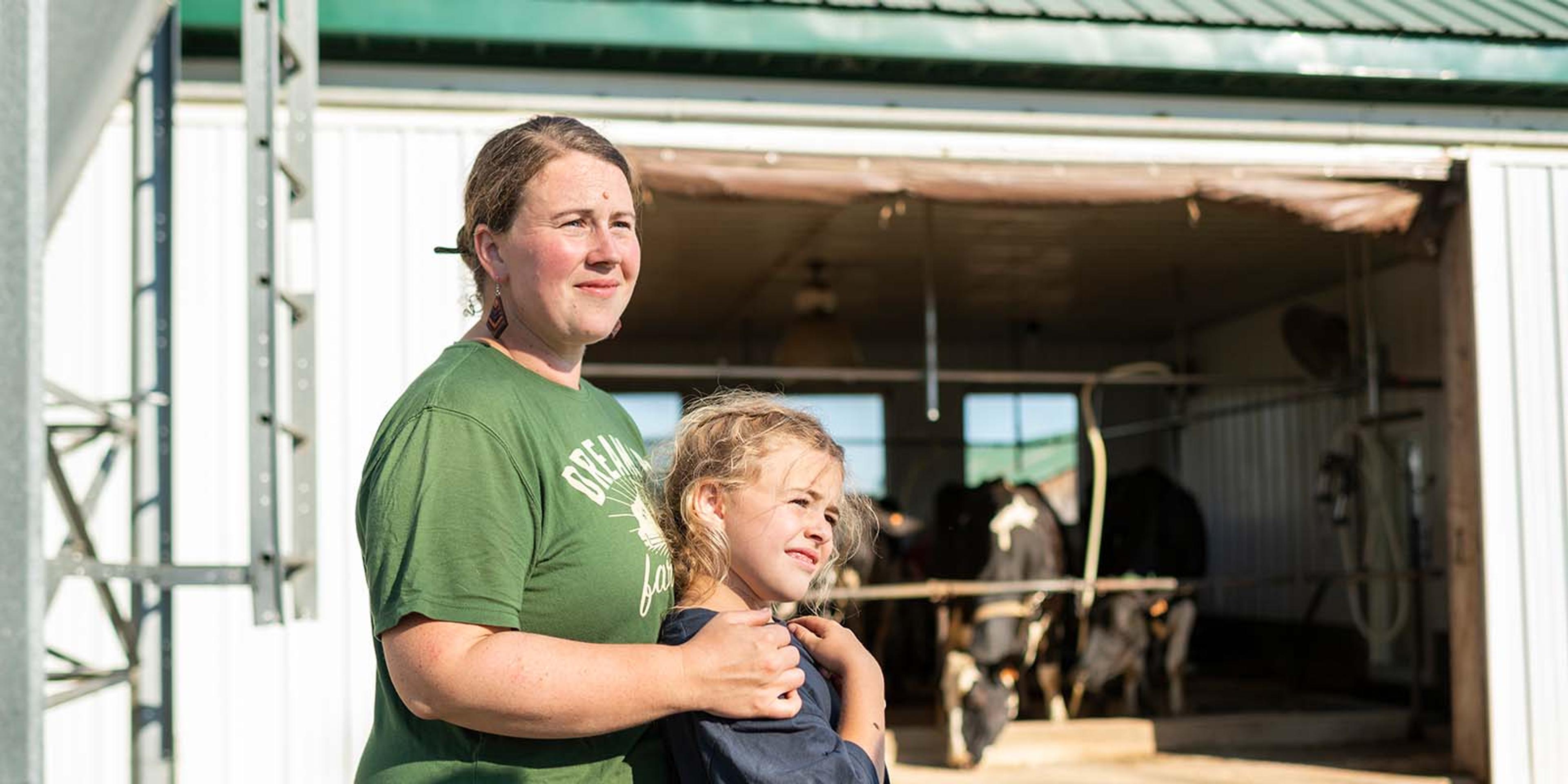 Mom and daughter stand in front of a barn.