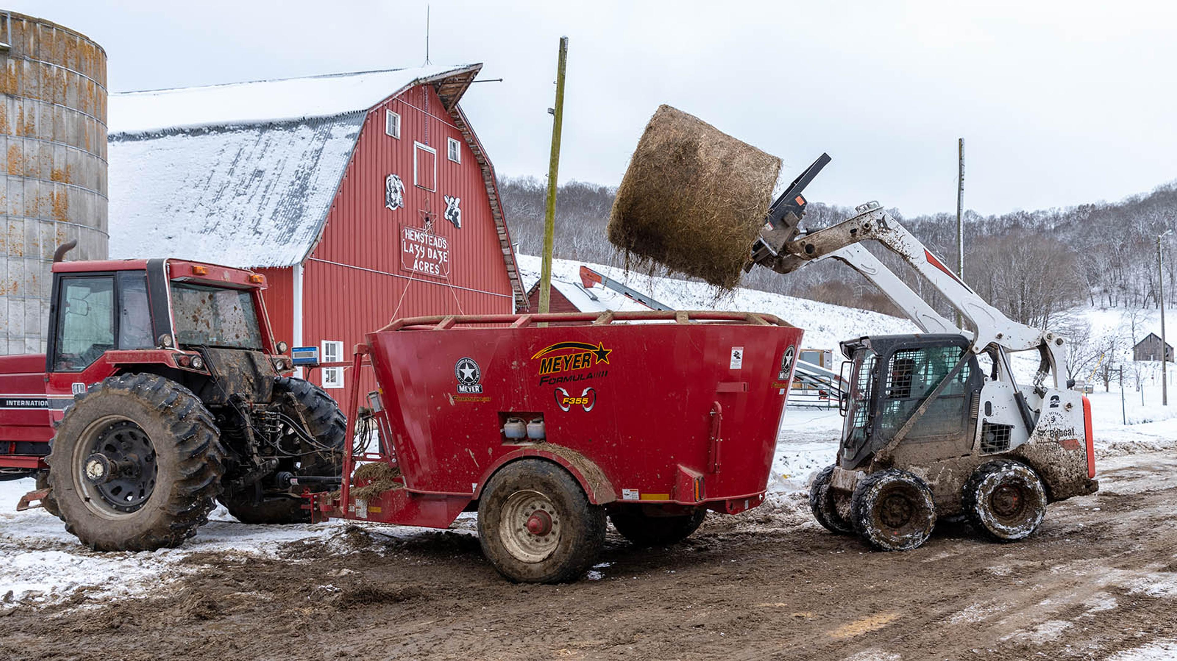 Using the end-loader to lift a round hay bale into a trailer pulled by a tractor.