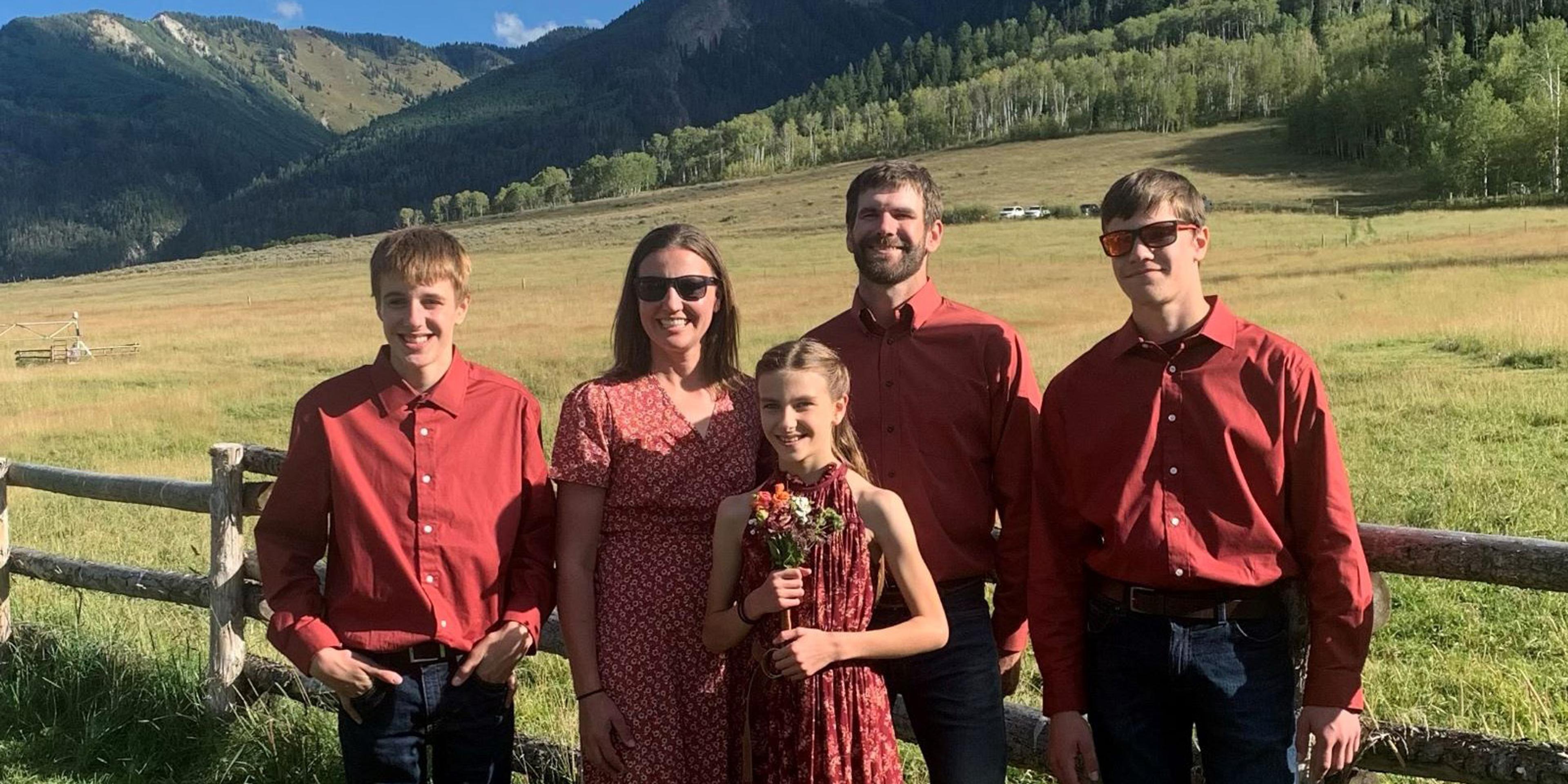 Five members of the Zweber family pose in front of a fence with mountains in the background.