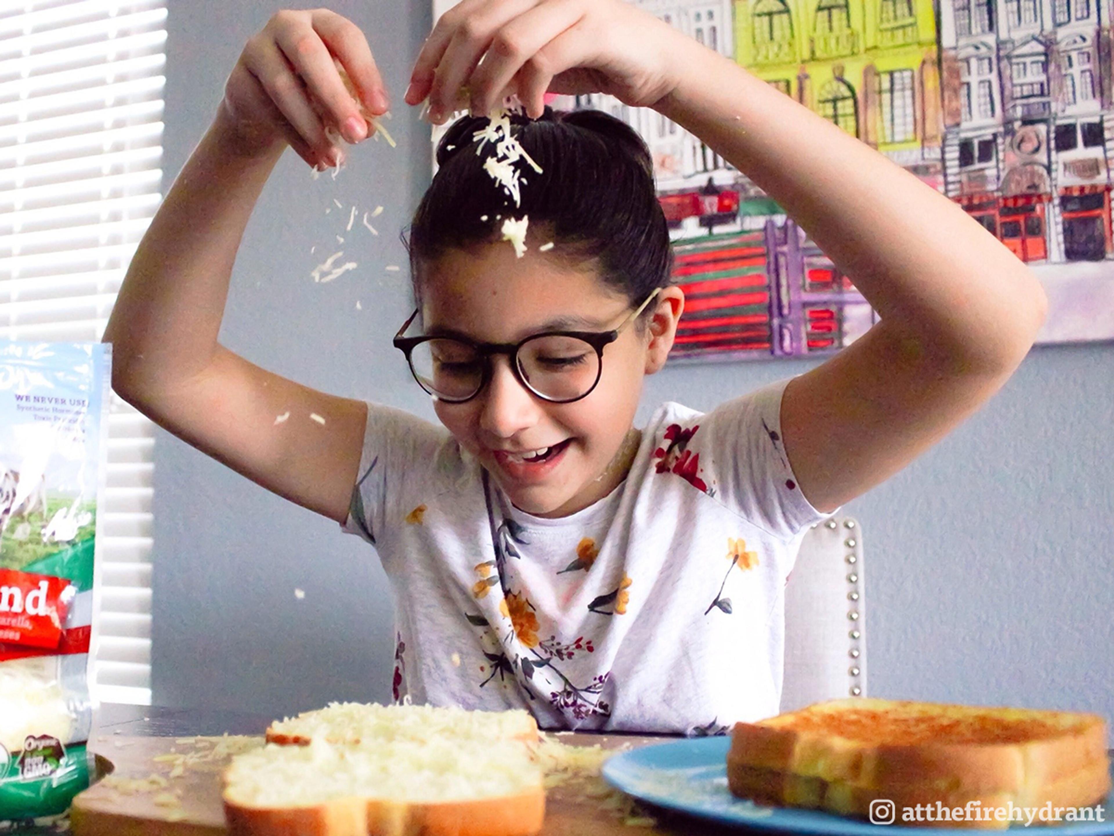 Preteen girl in glasses puts together a grilled cheese sandwich.