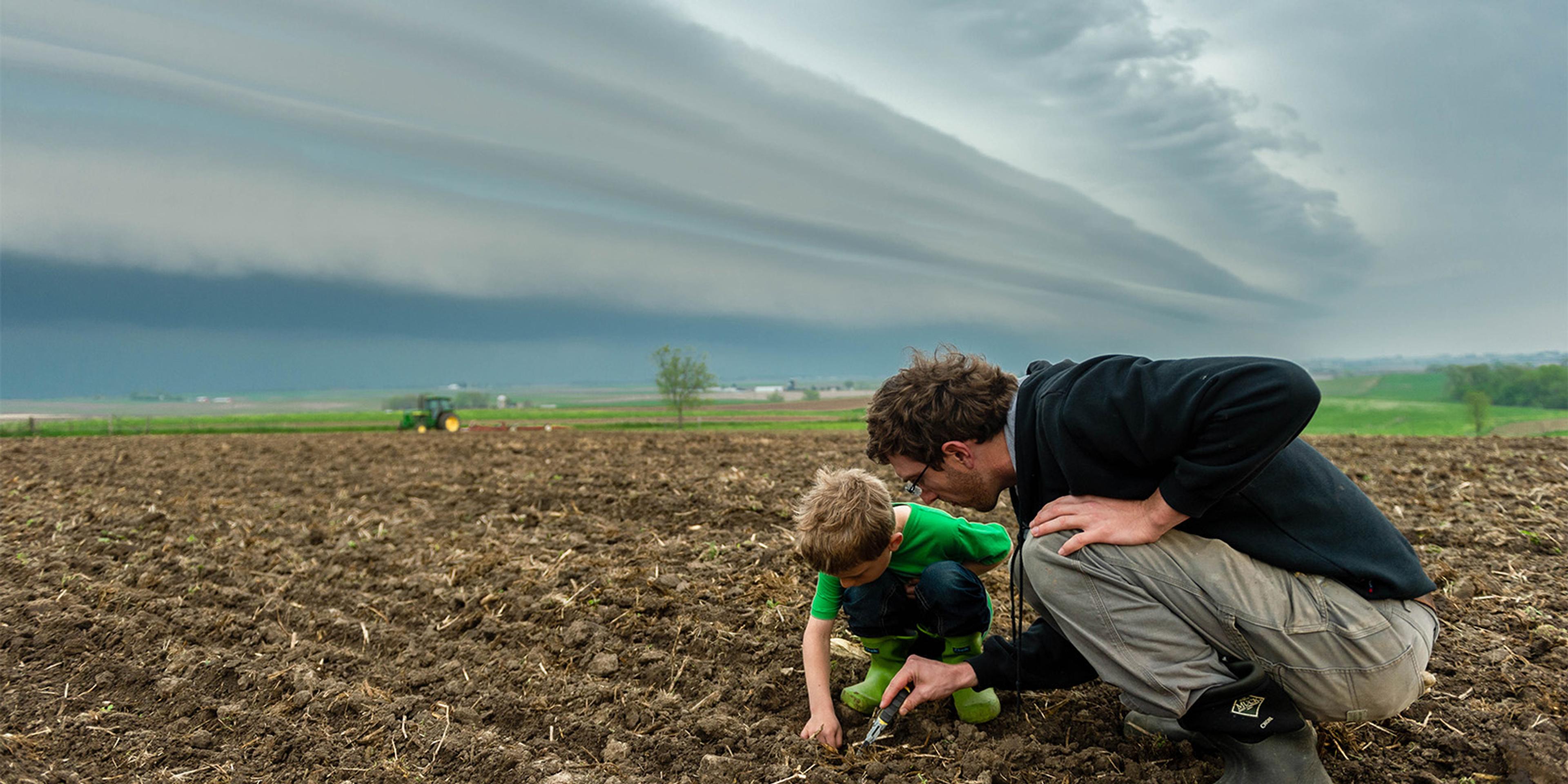A dad and son kneel to inspect the soil on their Wisconsin farm.