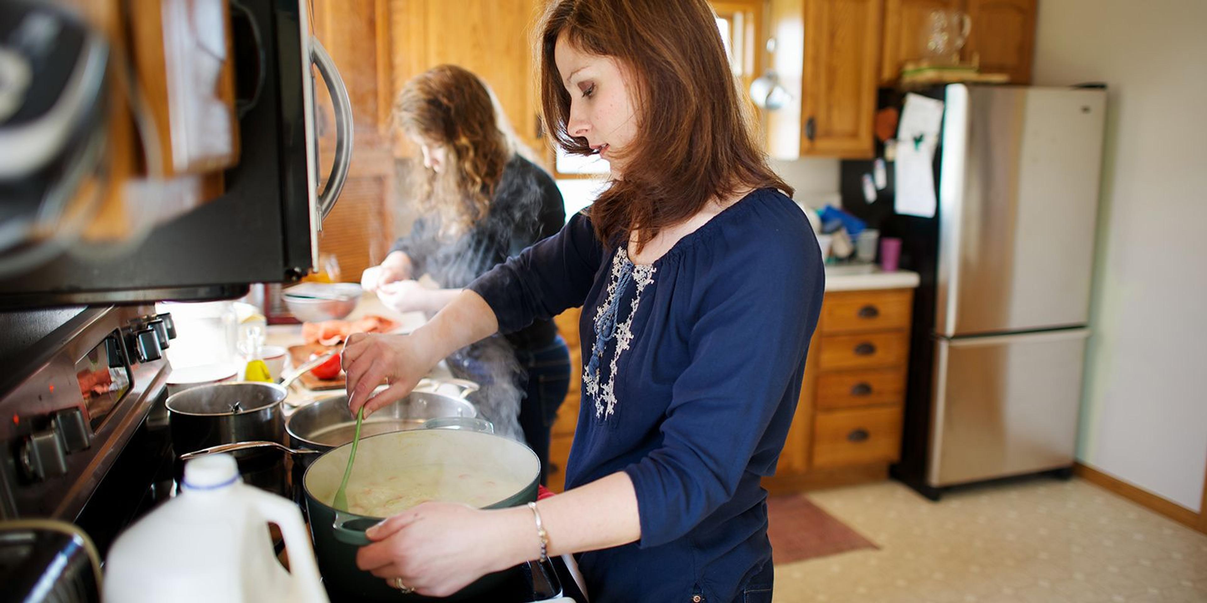 Mom and daughter prepare leftovers in the kitchen and warm up soup on the stove.