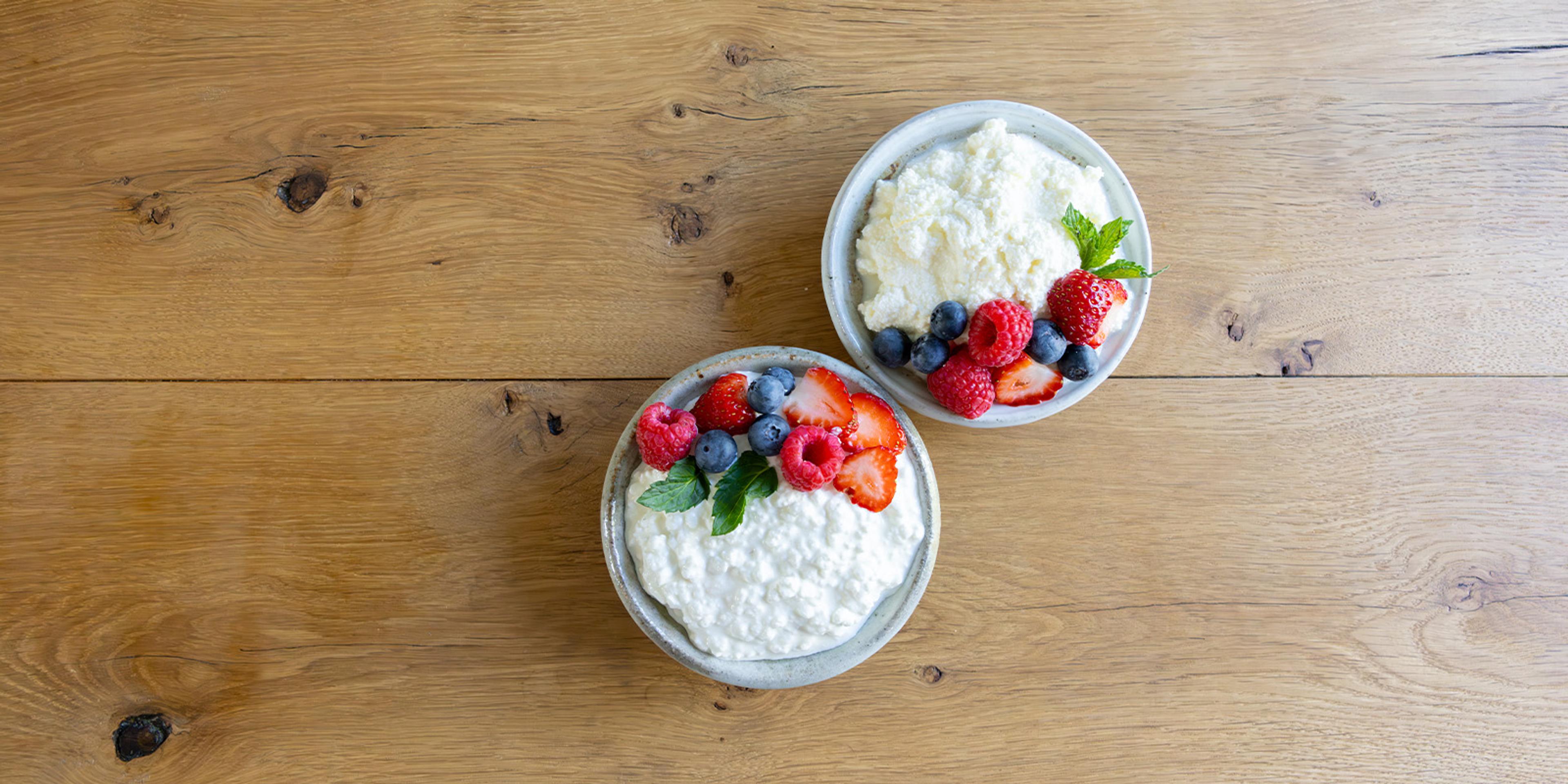  A bowl of organic cottage cheese and organic ricotta cheeses with fruit on a table.