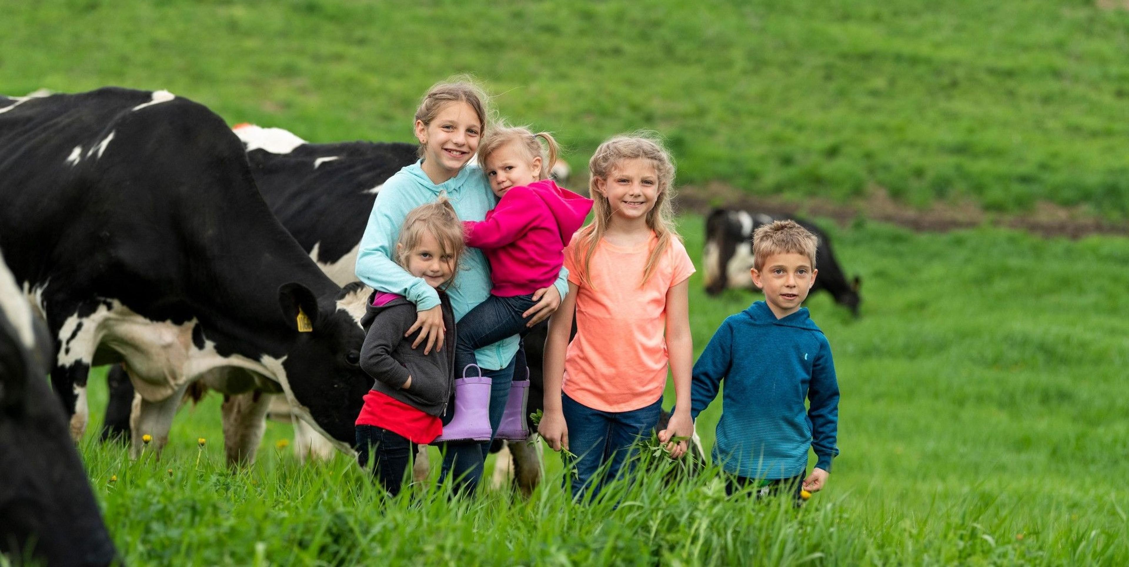 Five children stand in a field with cows on pasture.