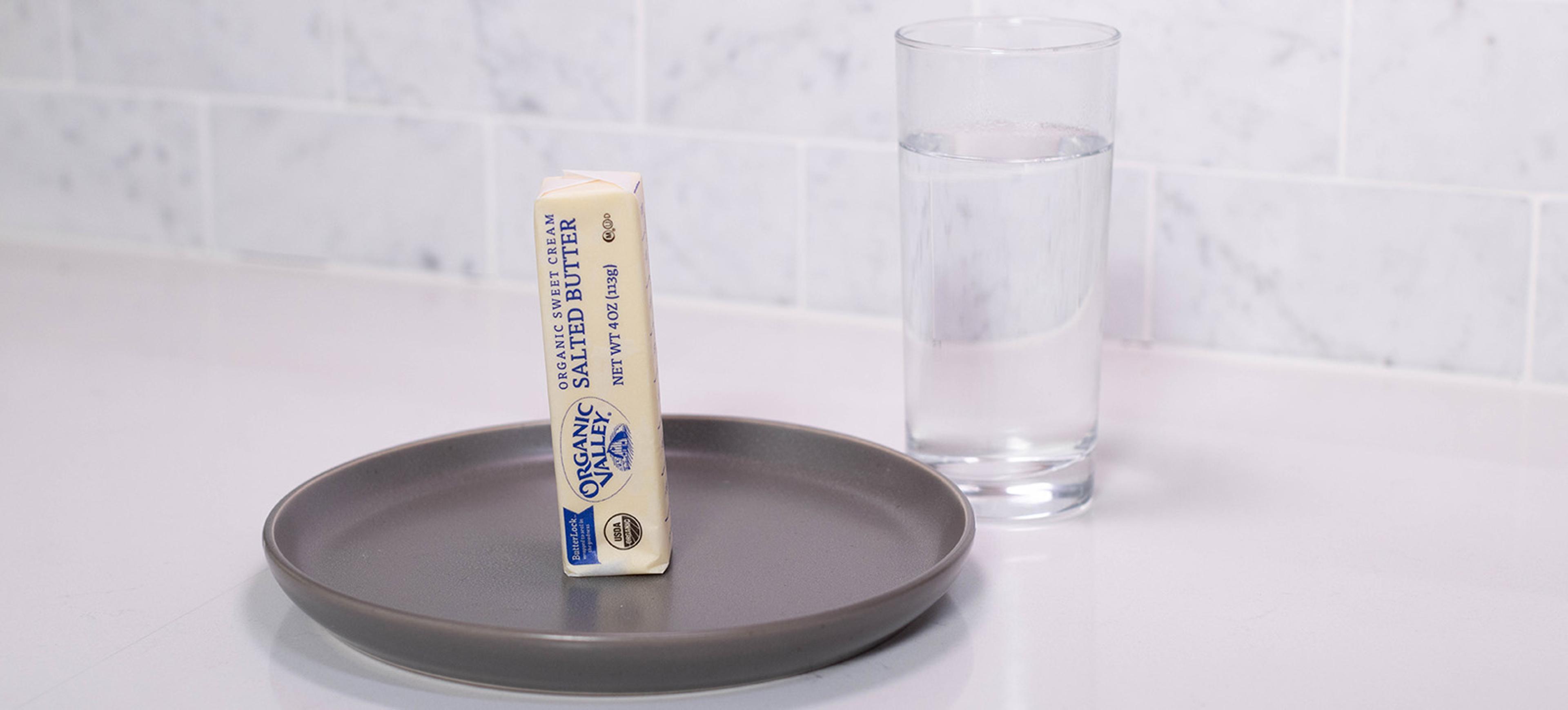 A stick of butter next to a glass of water.