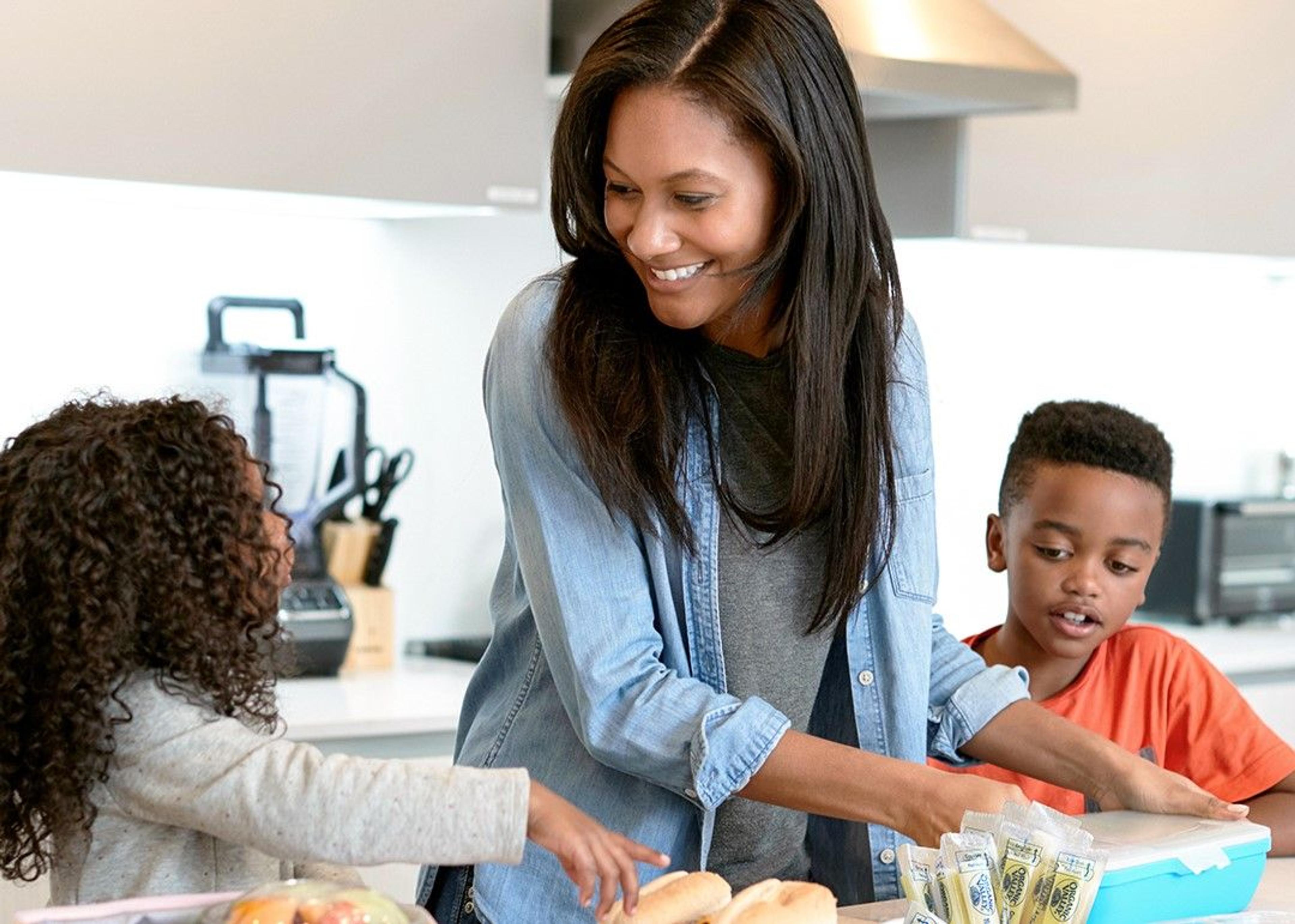 A mother talking with her two children while packing their lunch. 