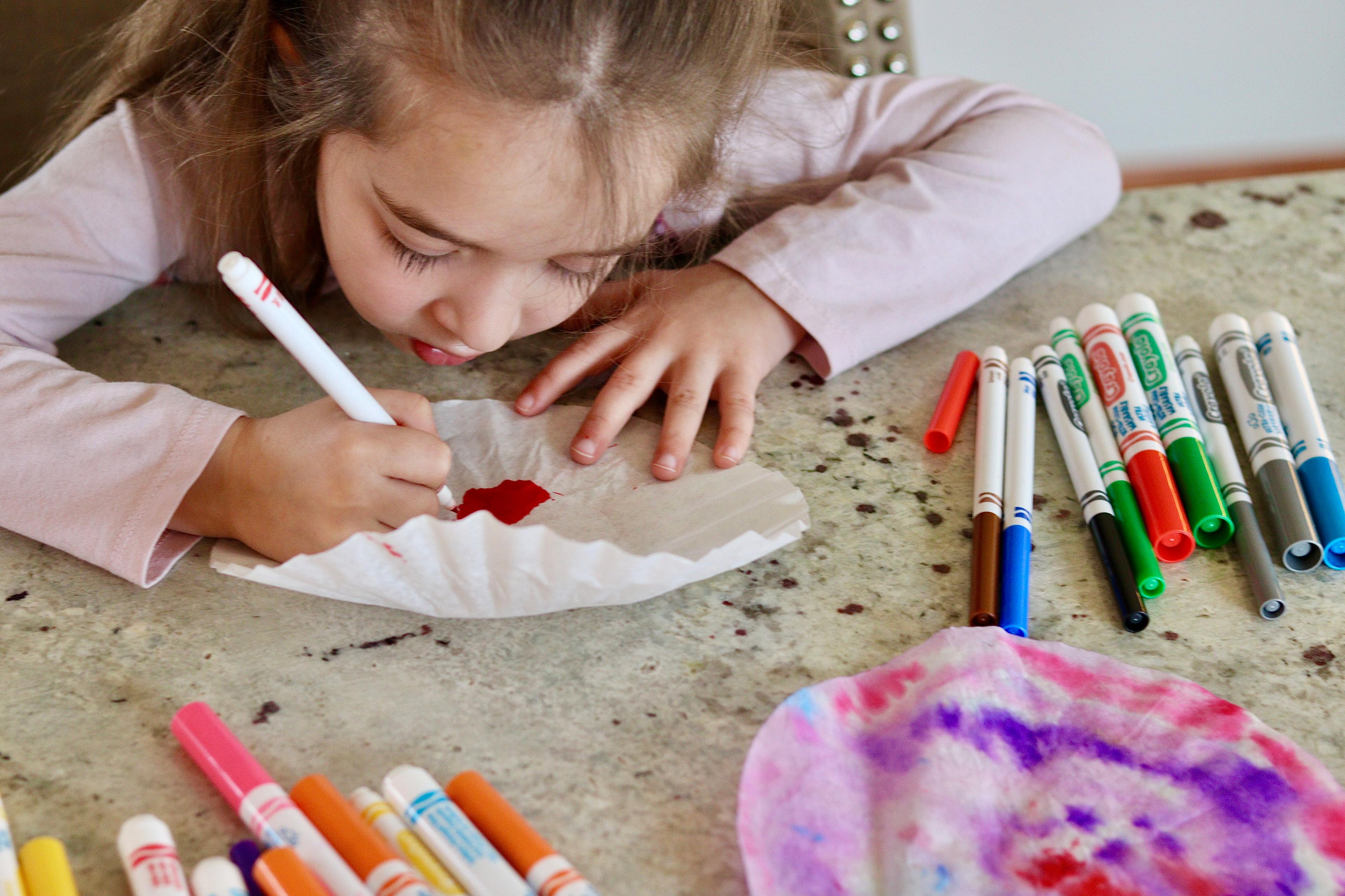 A girl colors a coffee filter.