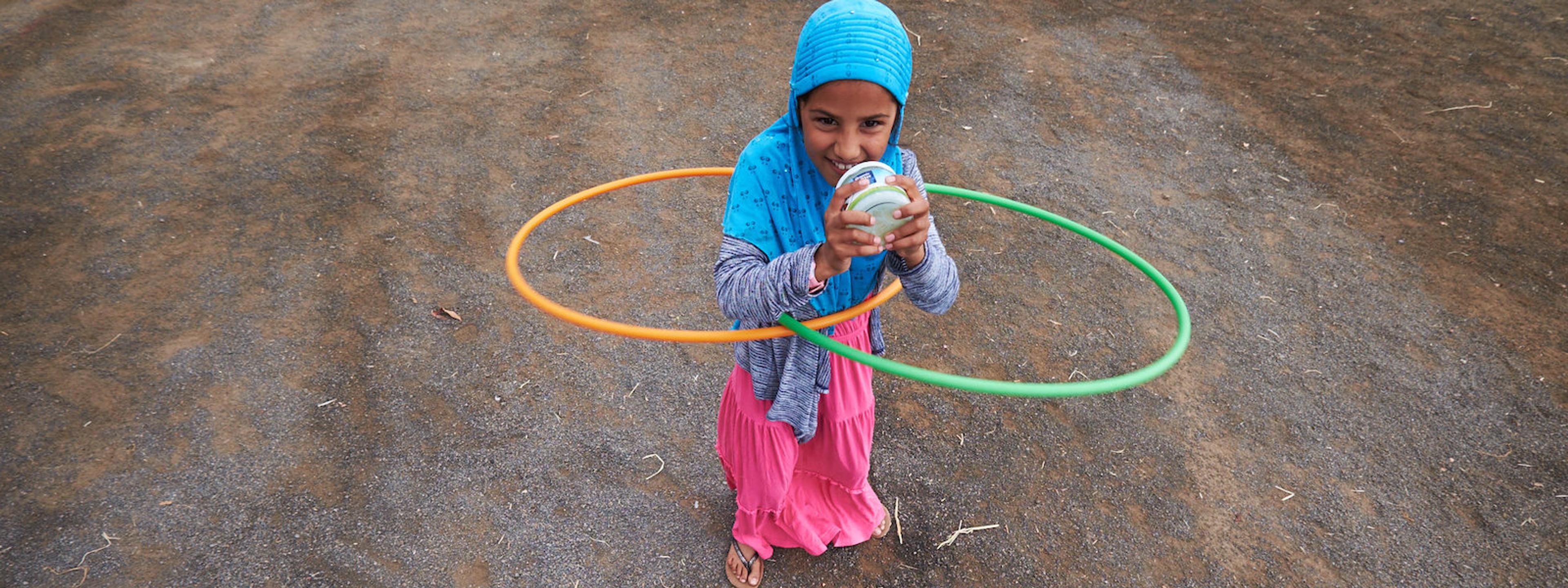 A girl shakes up a jar of butter while hula hooping.