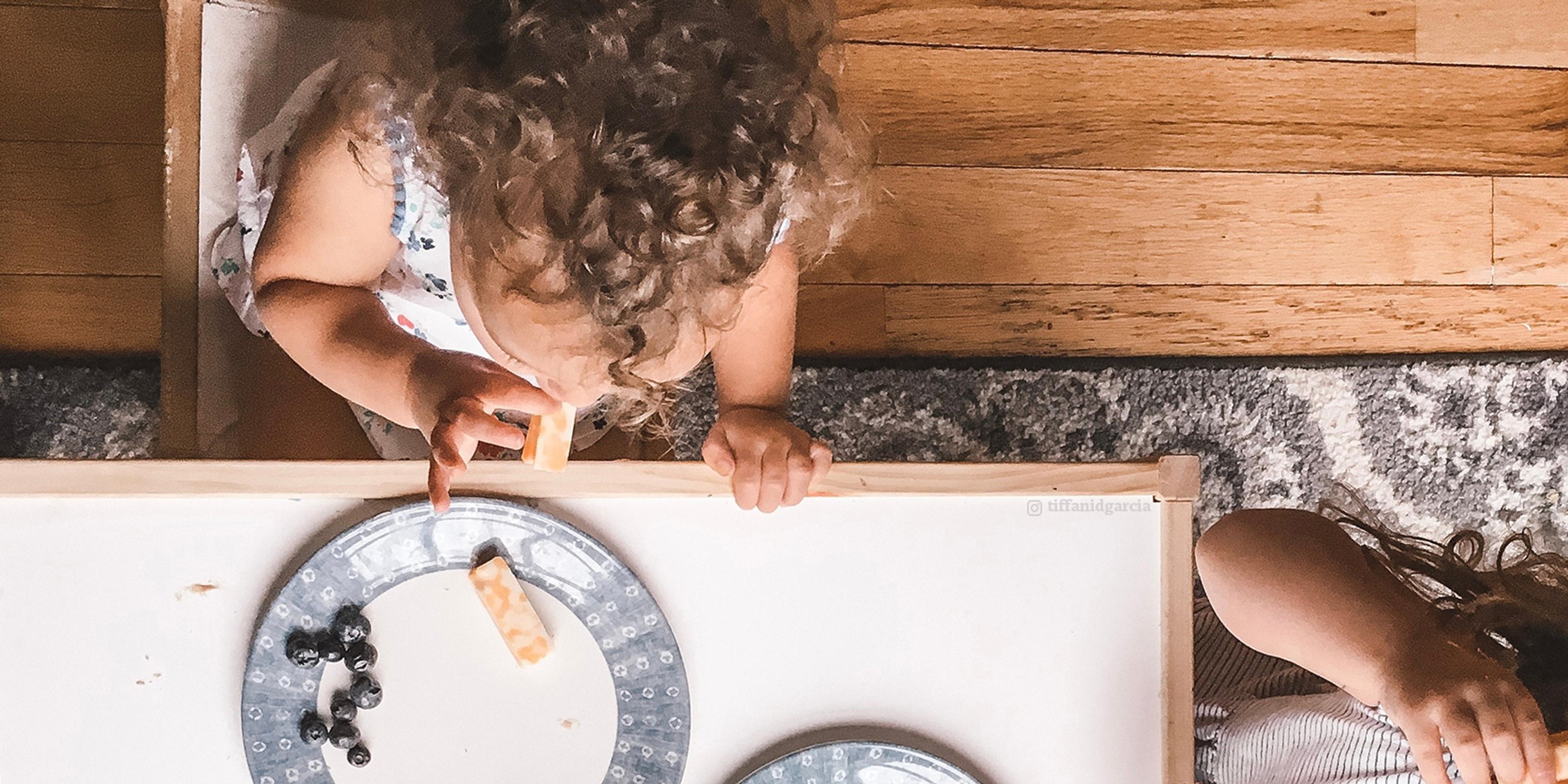 Little girl with curly hair snacks on Colby jack cheese sticks and blueberries.