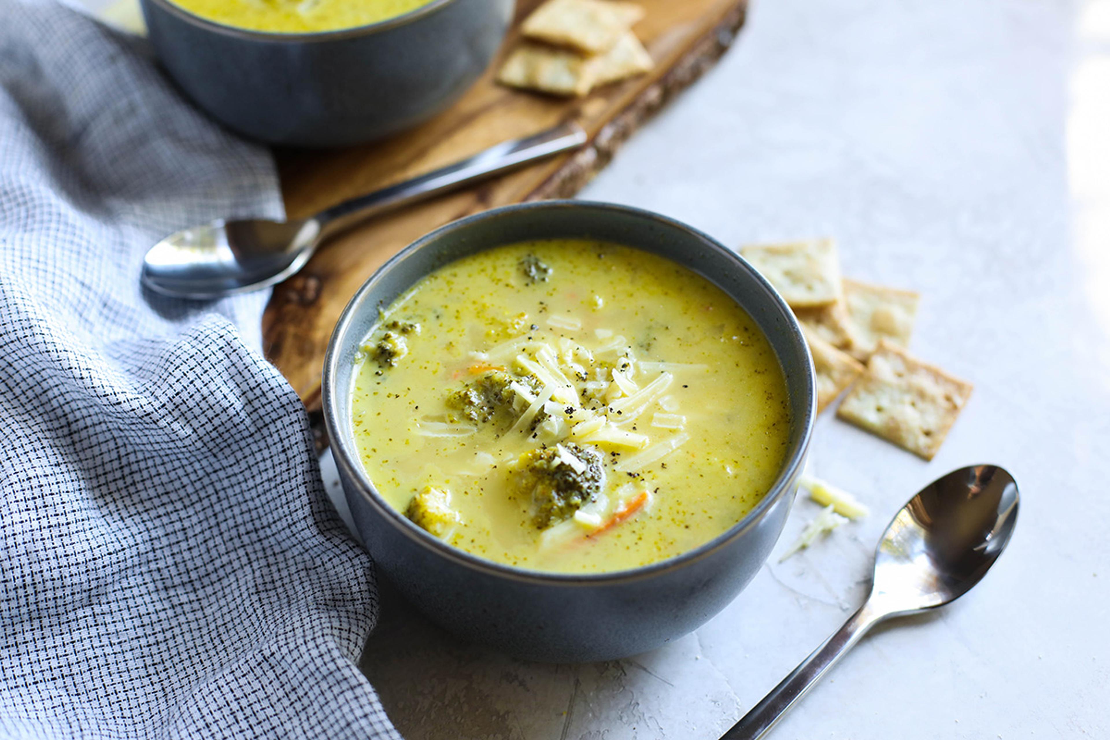 A bowl of broccoli cheese soup with some broccoli florets peeking out, and all topped with shredded cheese.