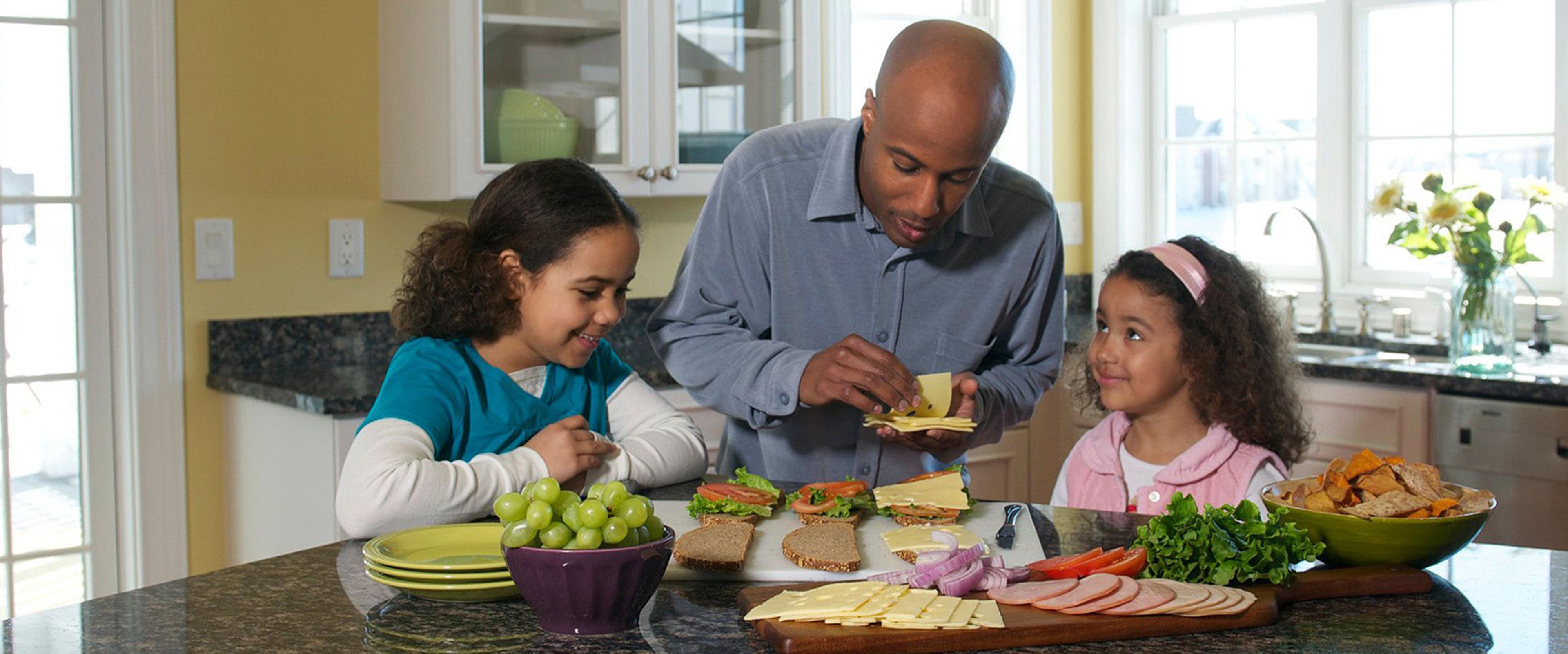 A dad makes deli sandwiches with two girls