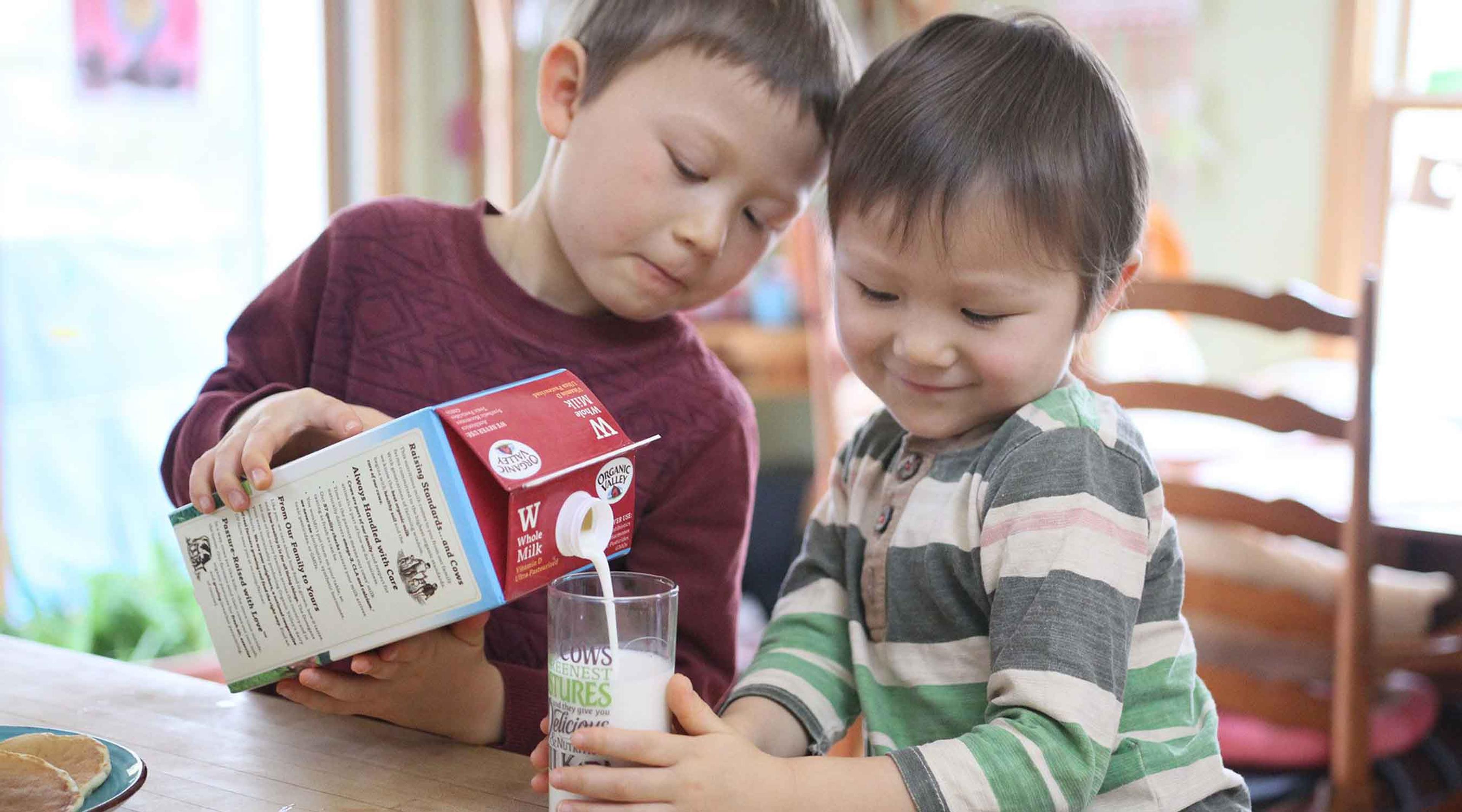 A boy pours organic milk into a glass.