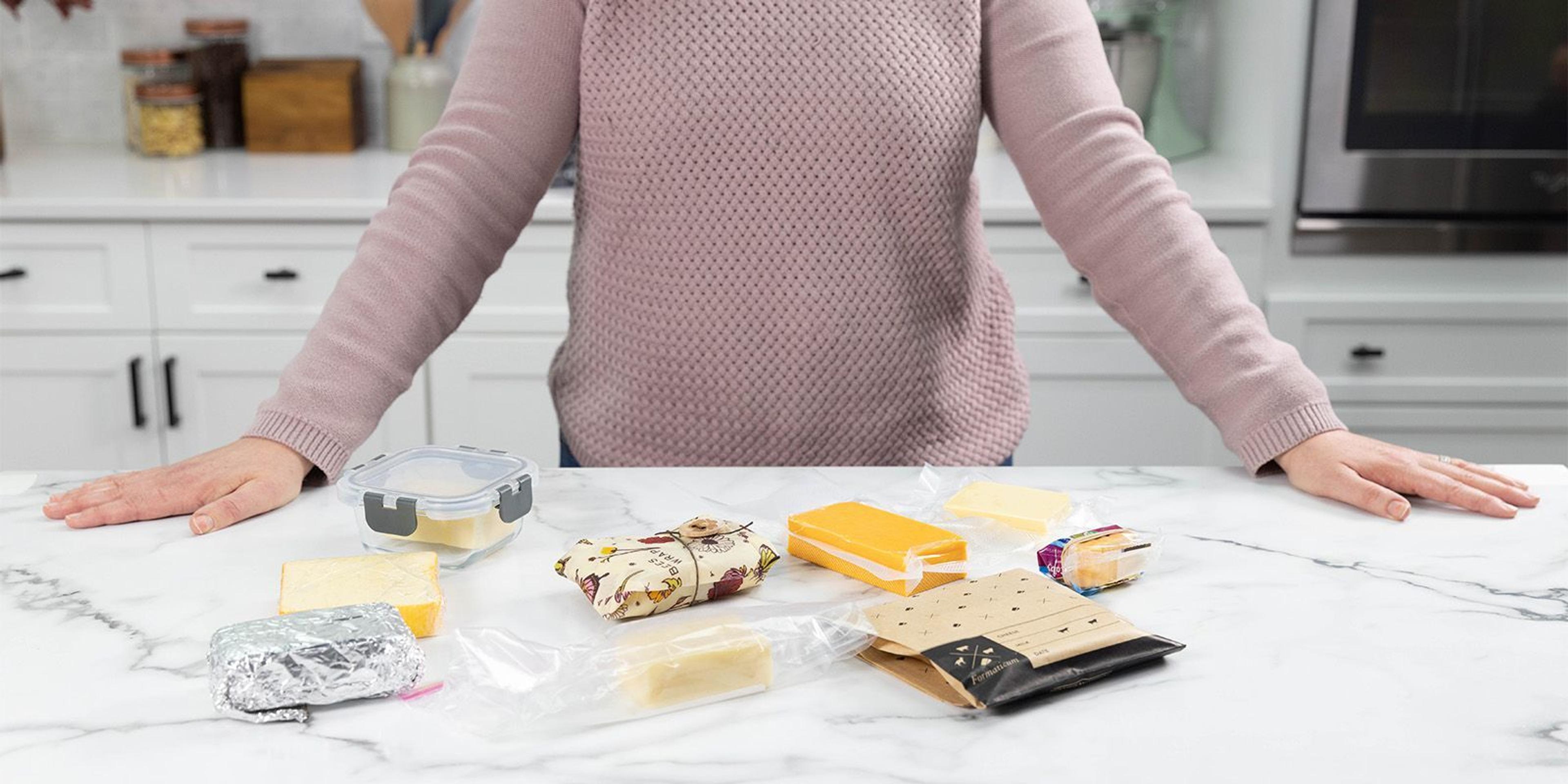 Cheese on the counter wrapped in various preservation methods such as aluminum foil, plastic and cheese paper.