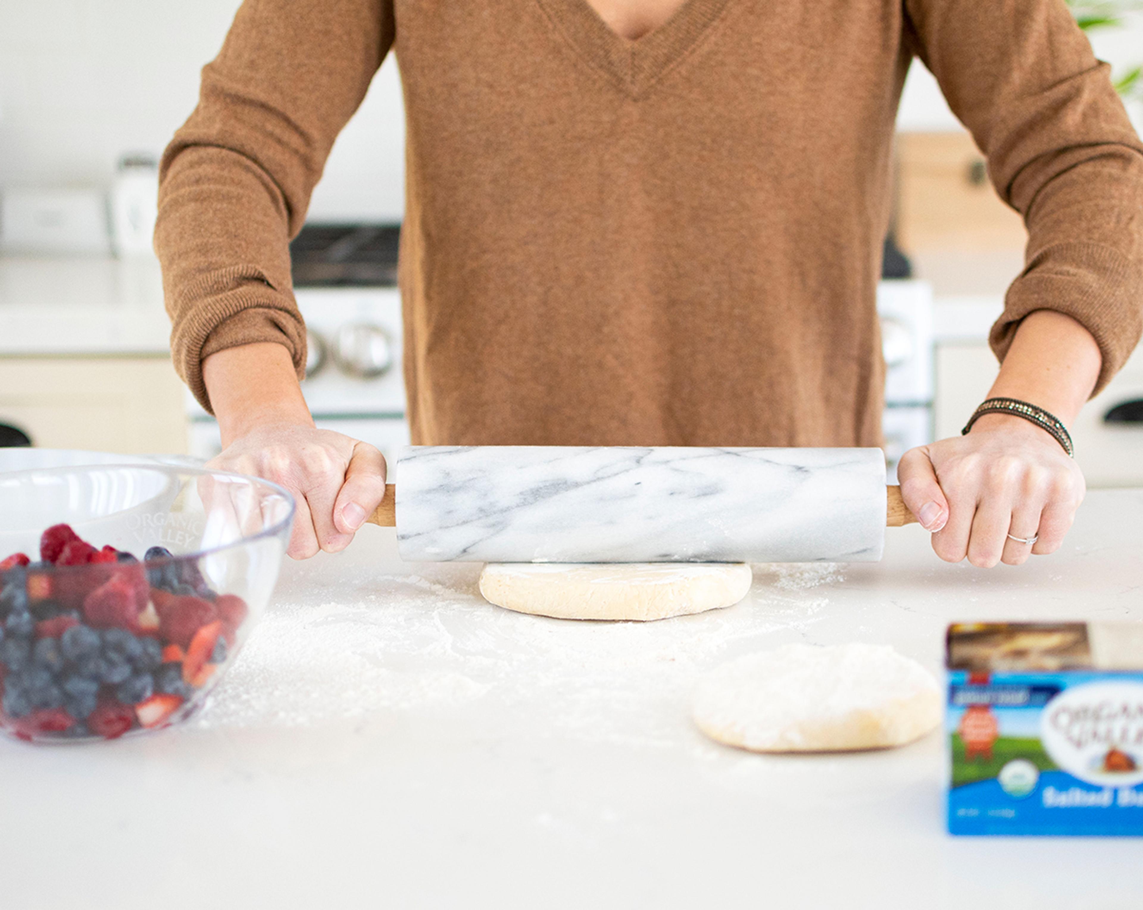 Woman rolling out pie dough on a counter.