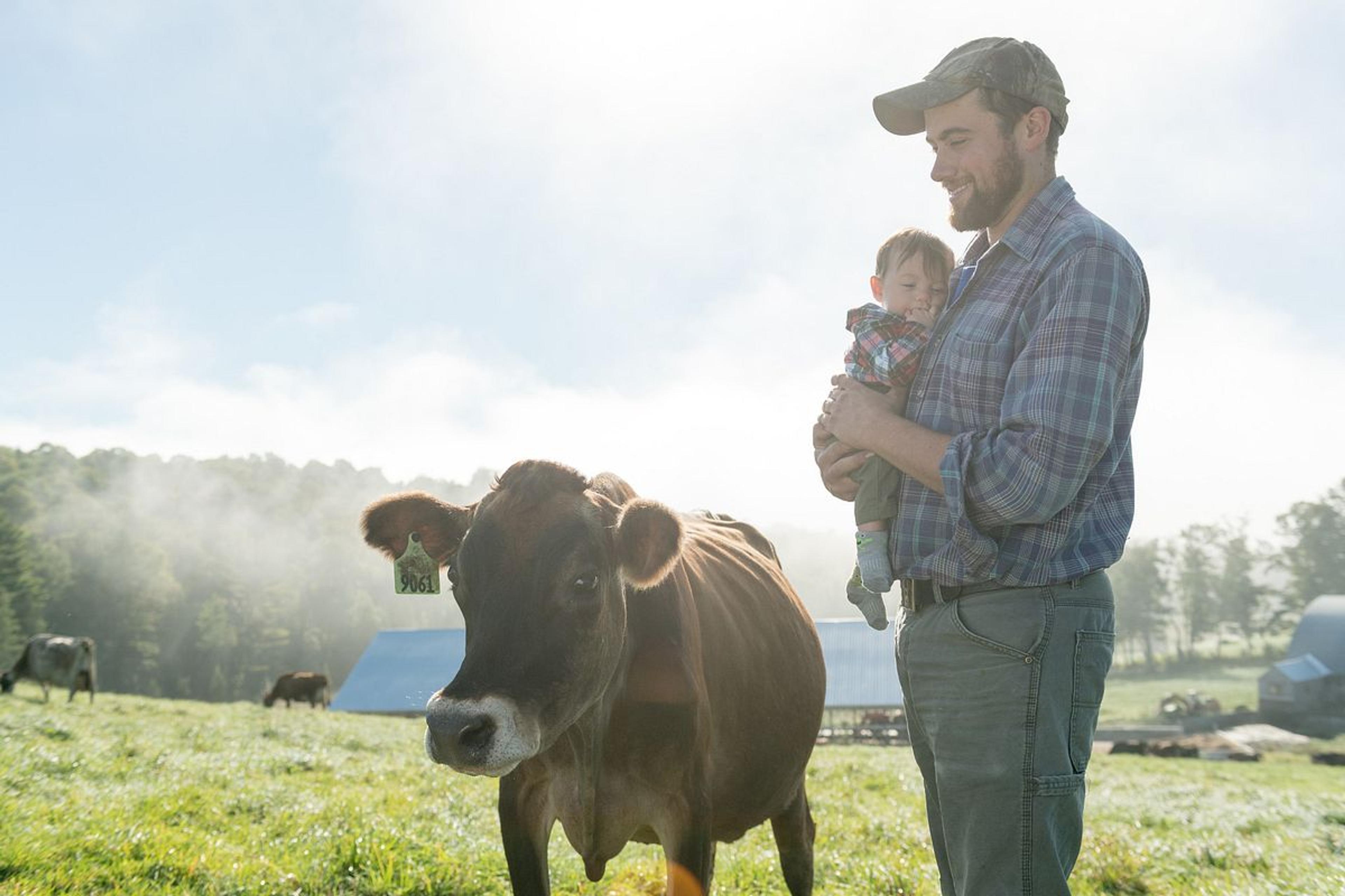 Henry Pearl holds his youngest son while next to a cow in their organic pasture on the Vermont farm.