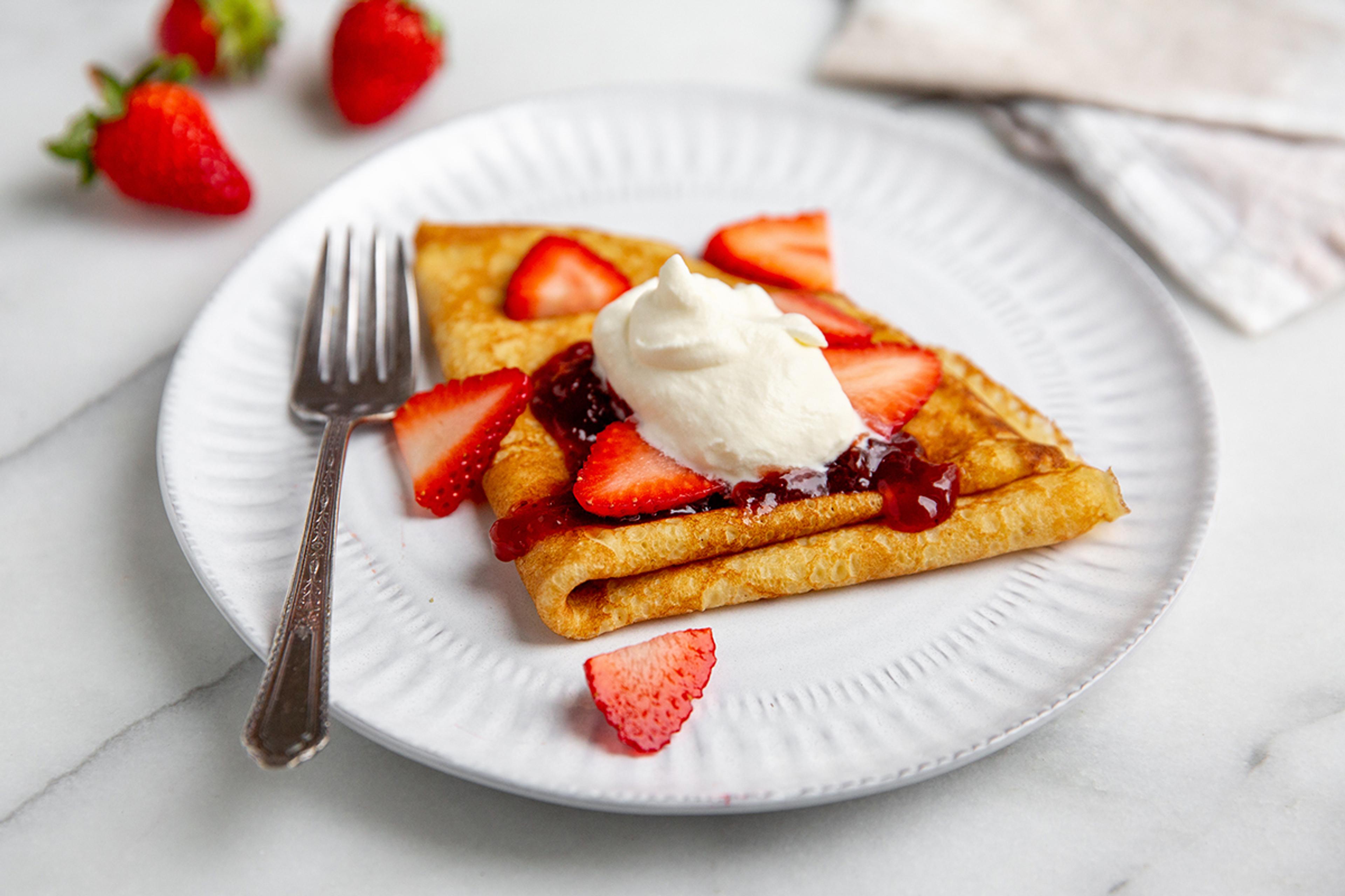 Sweet crepes topped with fresh homemade whipped cream, strawberries and jam.