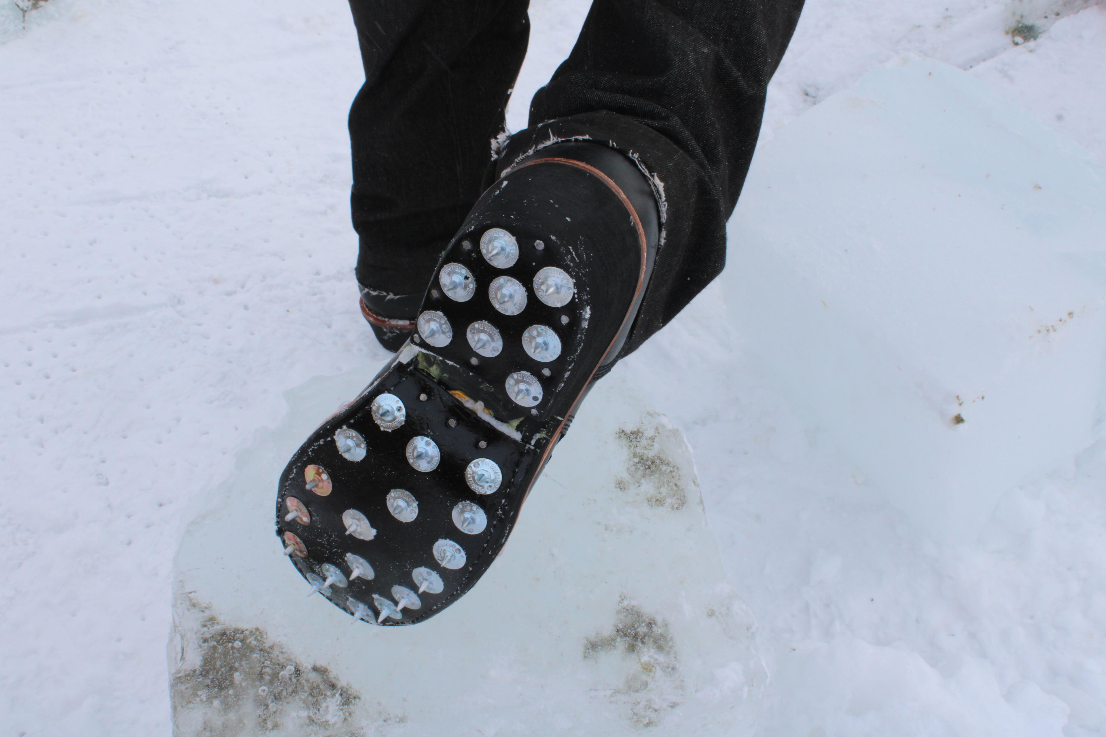A man puts his foot on a block of ice to show the cleats on the bottom.