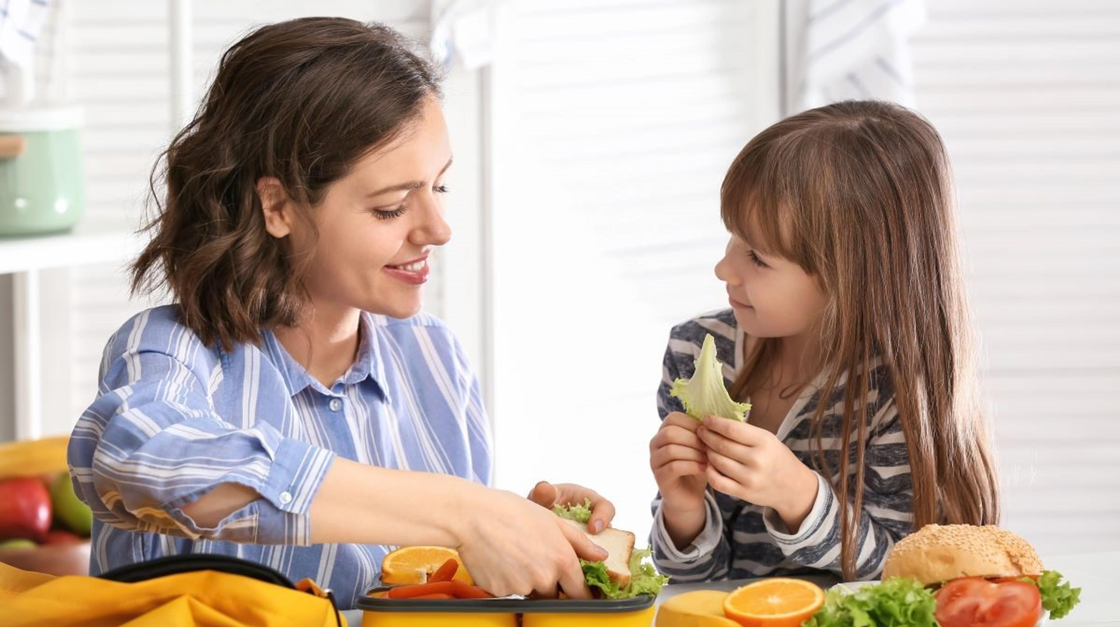 A woman and girl prep lettuce for sandwiches.