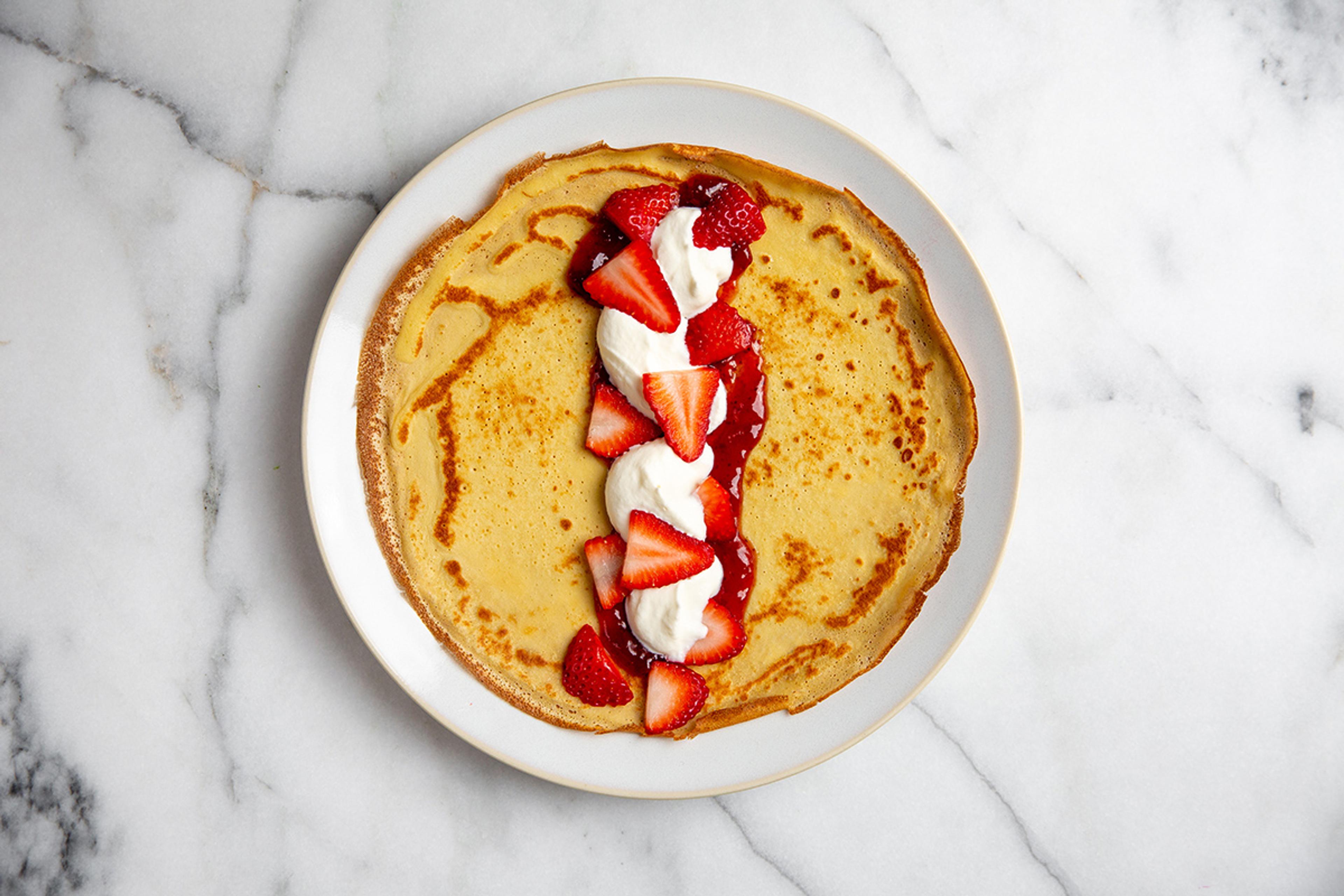 Open homemade crepe topped with fresh homemade whipped cream and strawberries.