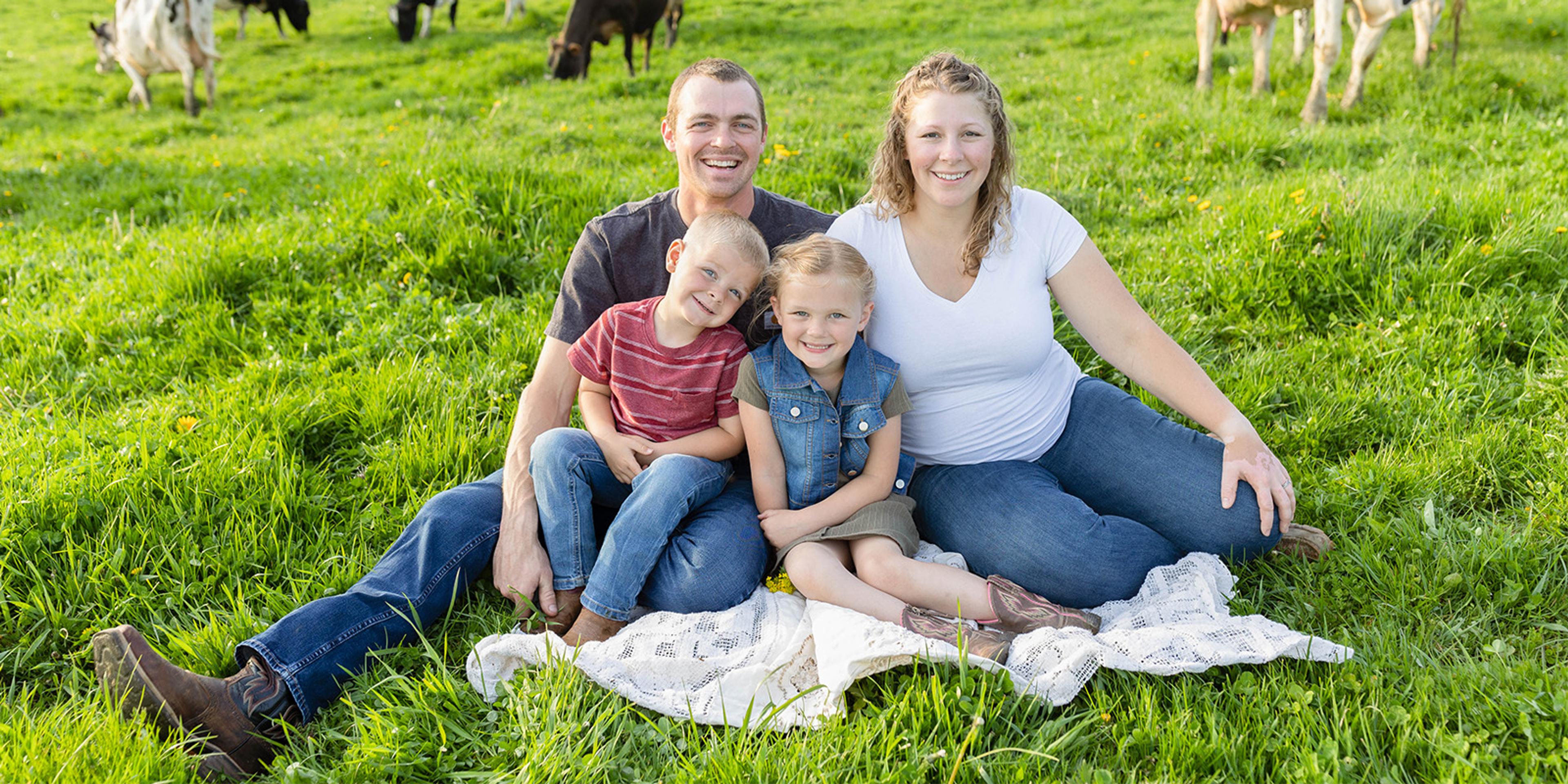 The Poole family, Bruce and Madeline with children George and Sophia, sits in a field at their New York farm as cows graze in the background.